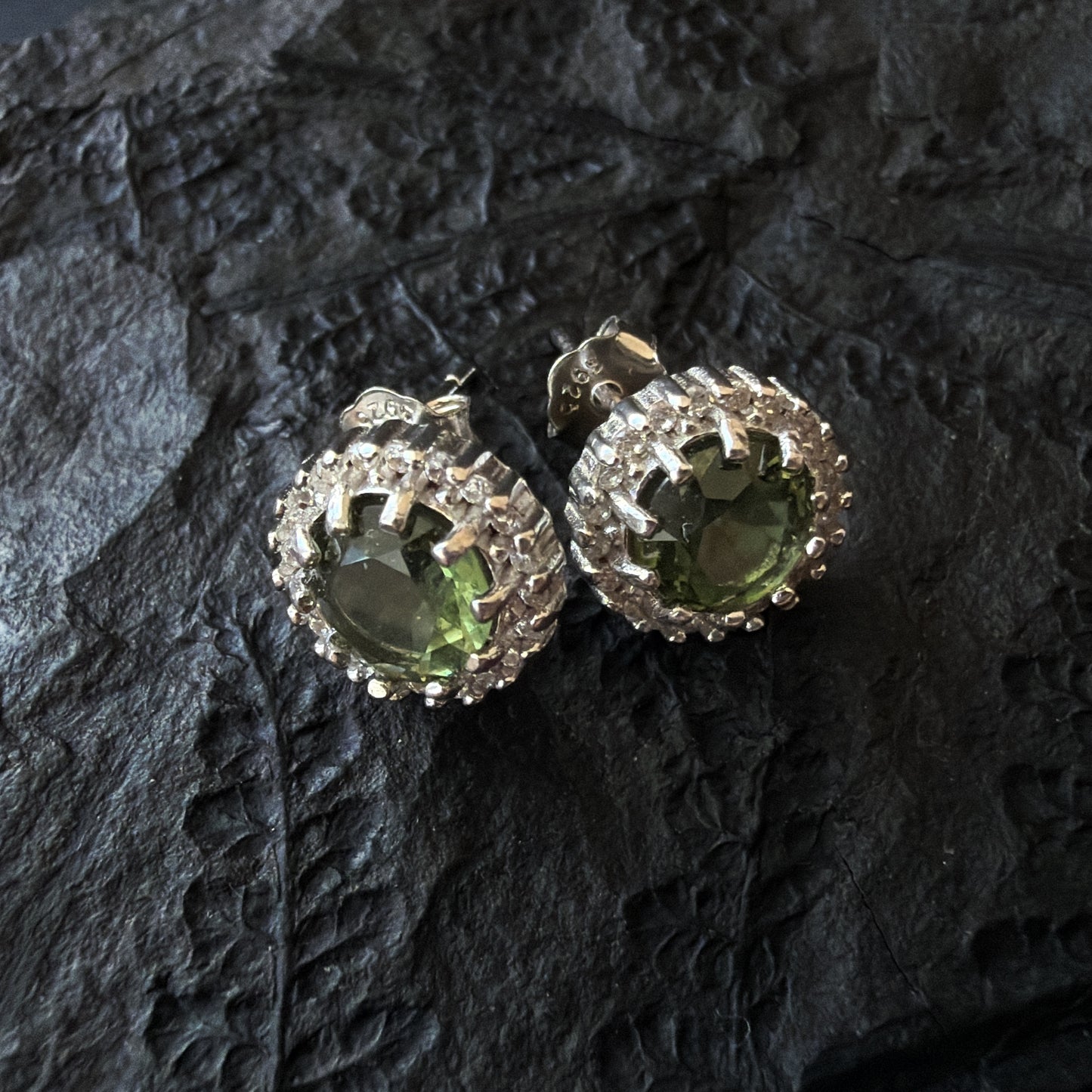 Pair of silver earrings with Moldavites on a dark textured surface
