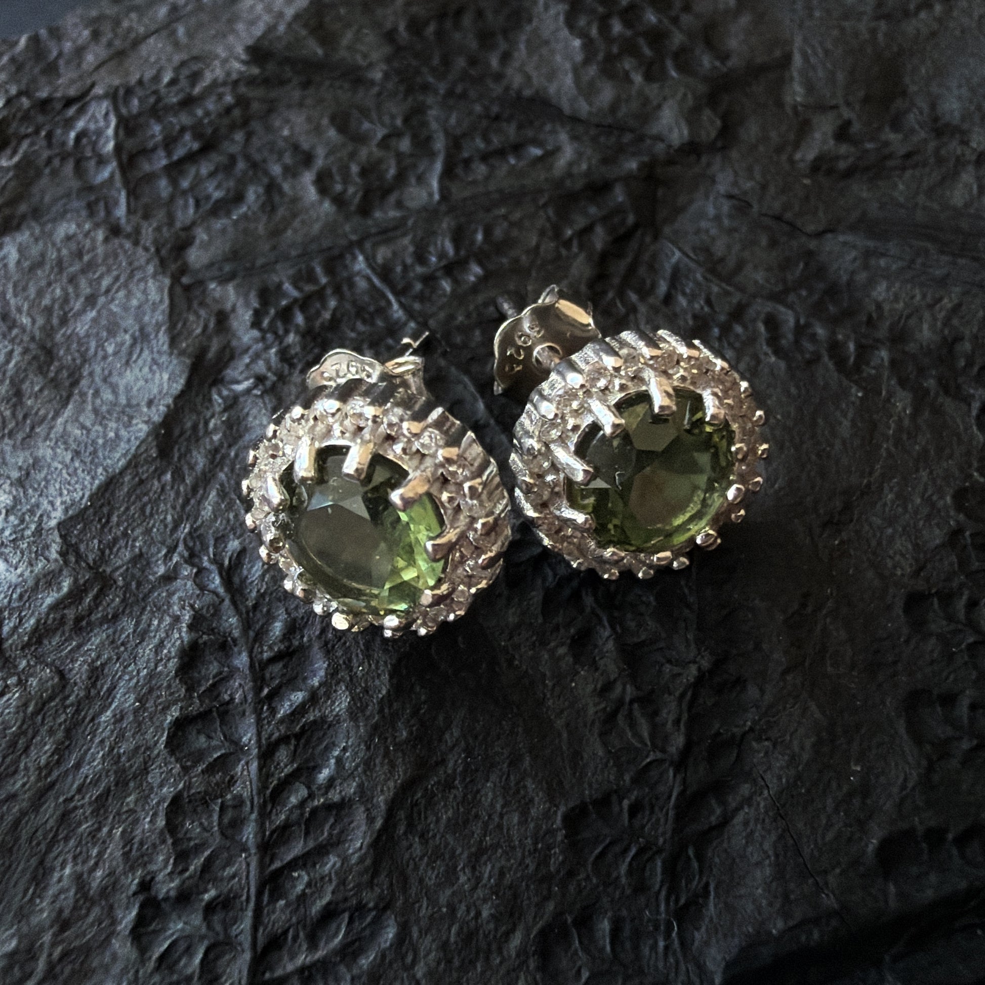 Pair of silver earrings with Moldavites on a dark textured surface