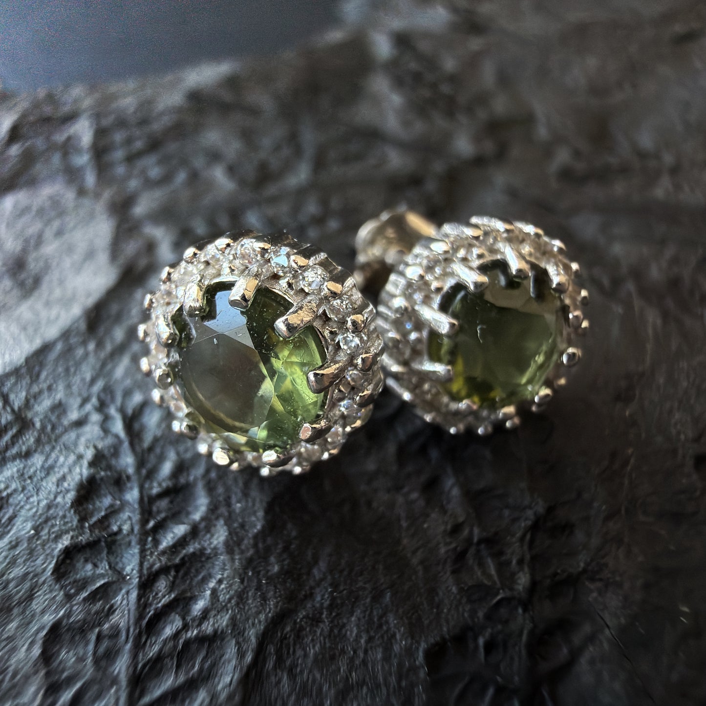 Pair of earrings with Moldavites diamond-like on a dark textured surface