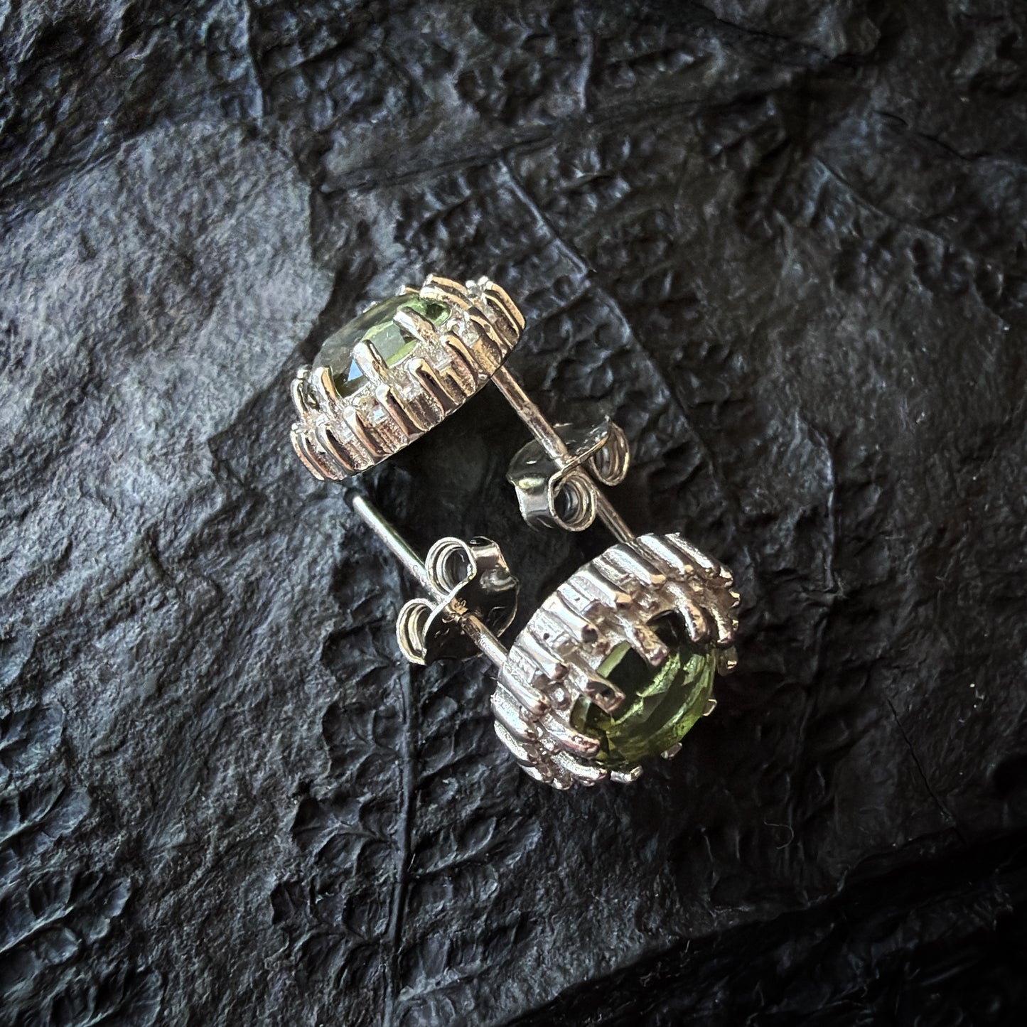 Pair of silver earrings with green gemstones on a dark textured surface