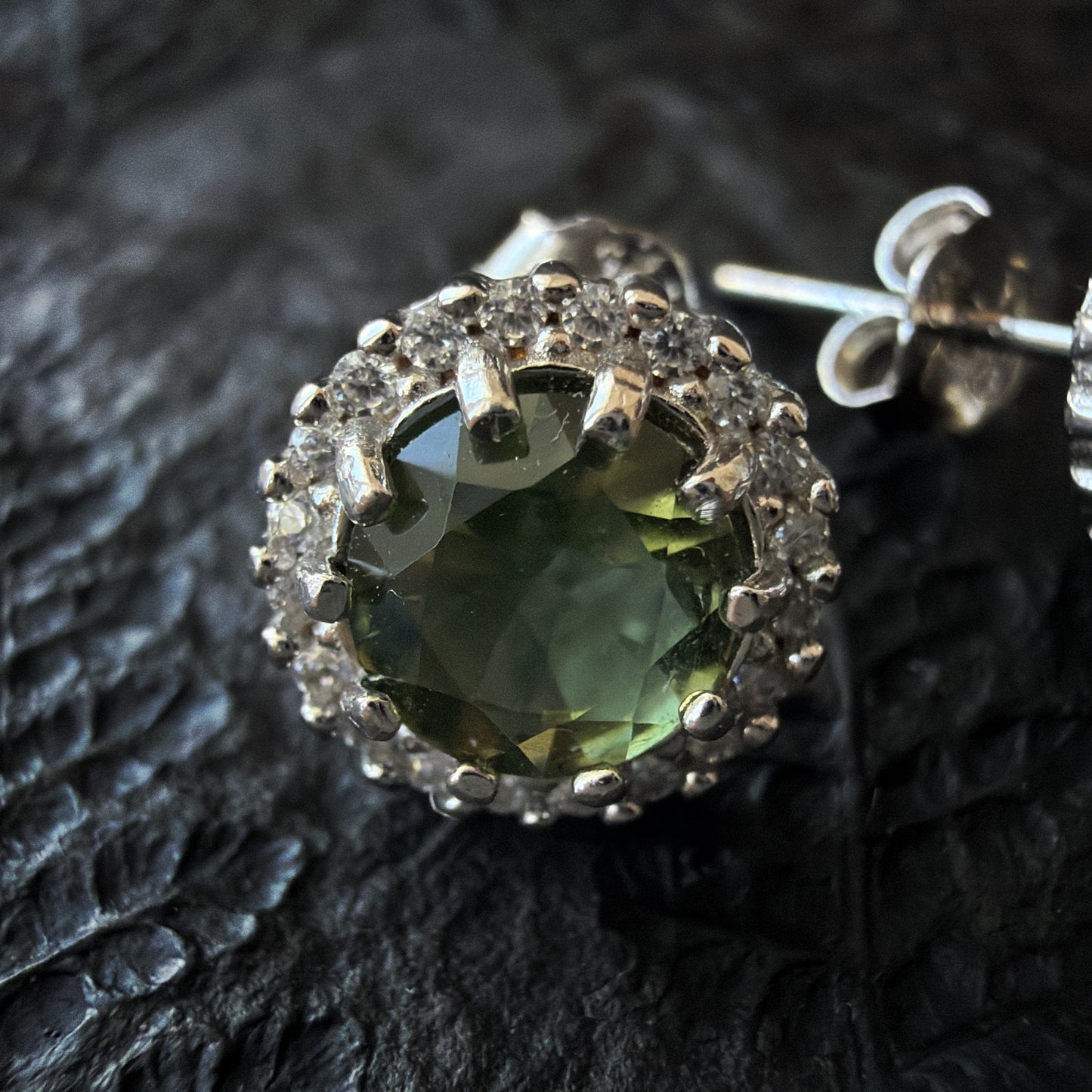Close-up of a Moldavite earring on a textured black surface