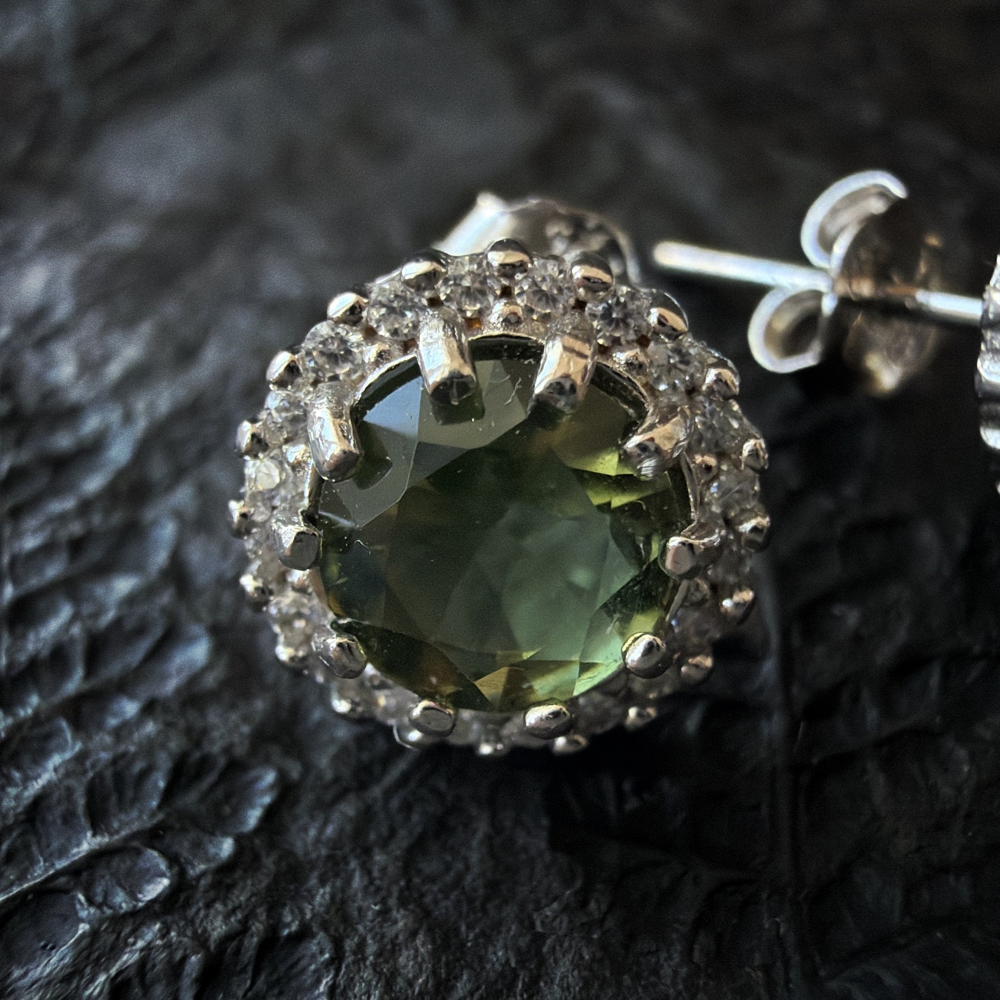 Close-up of a Moldavite earring on a textured black surface
