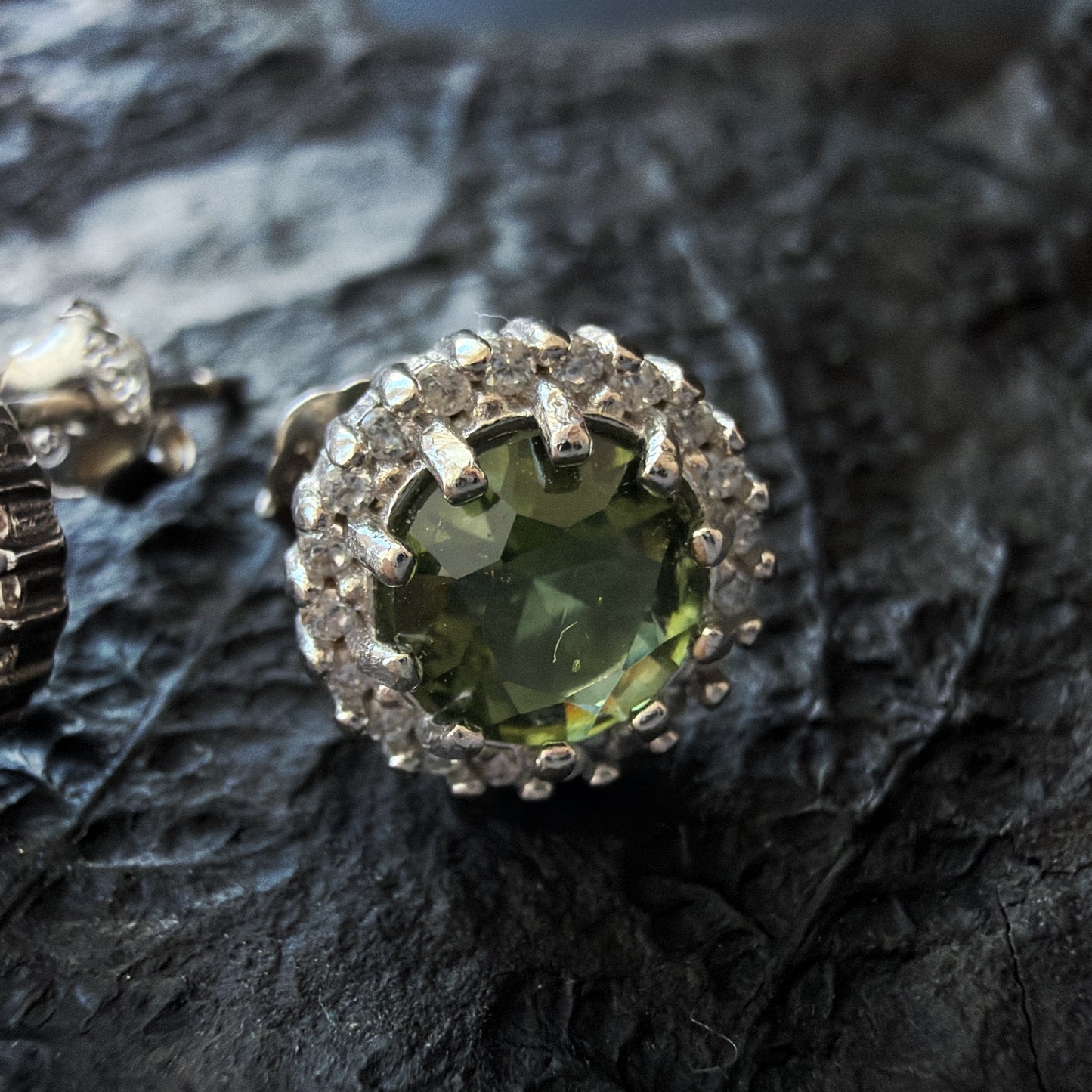 Close-up of a real moldavite earring on dark textured stone