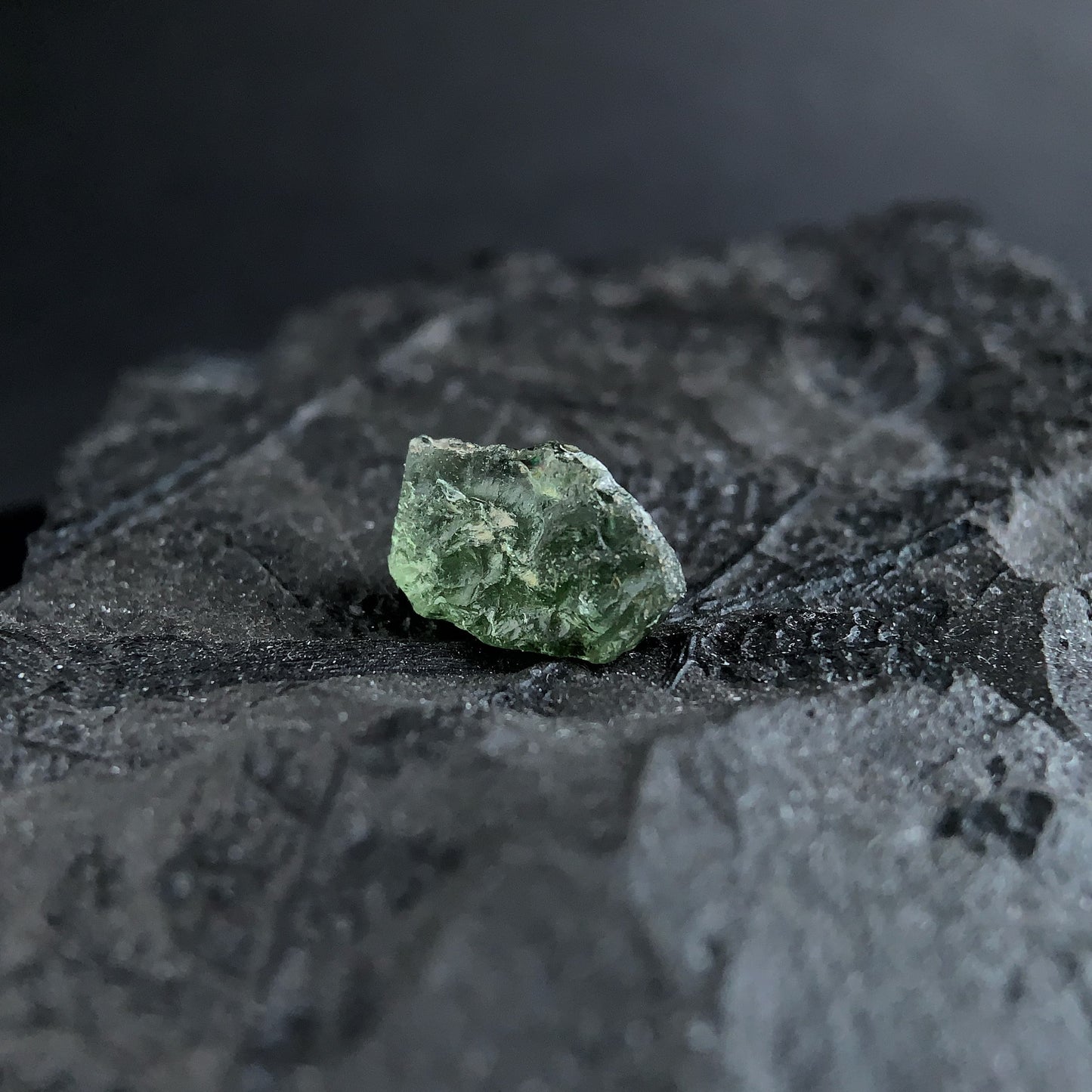 raw moldavite on a textured black surface with a dark background