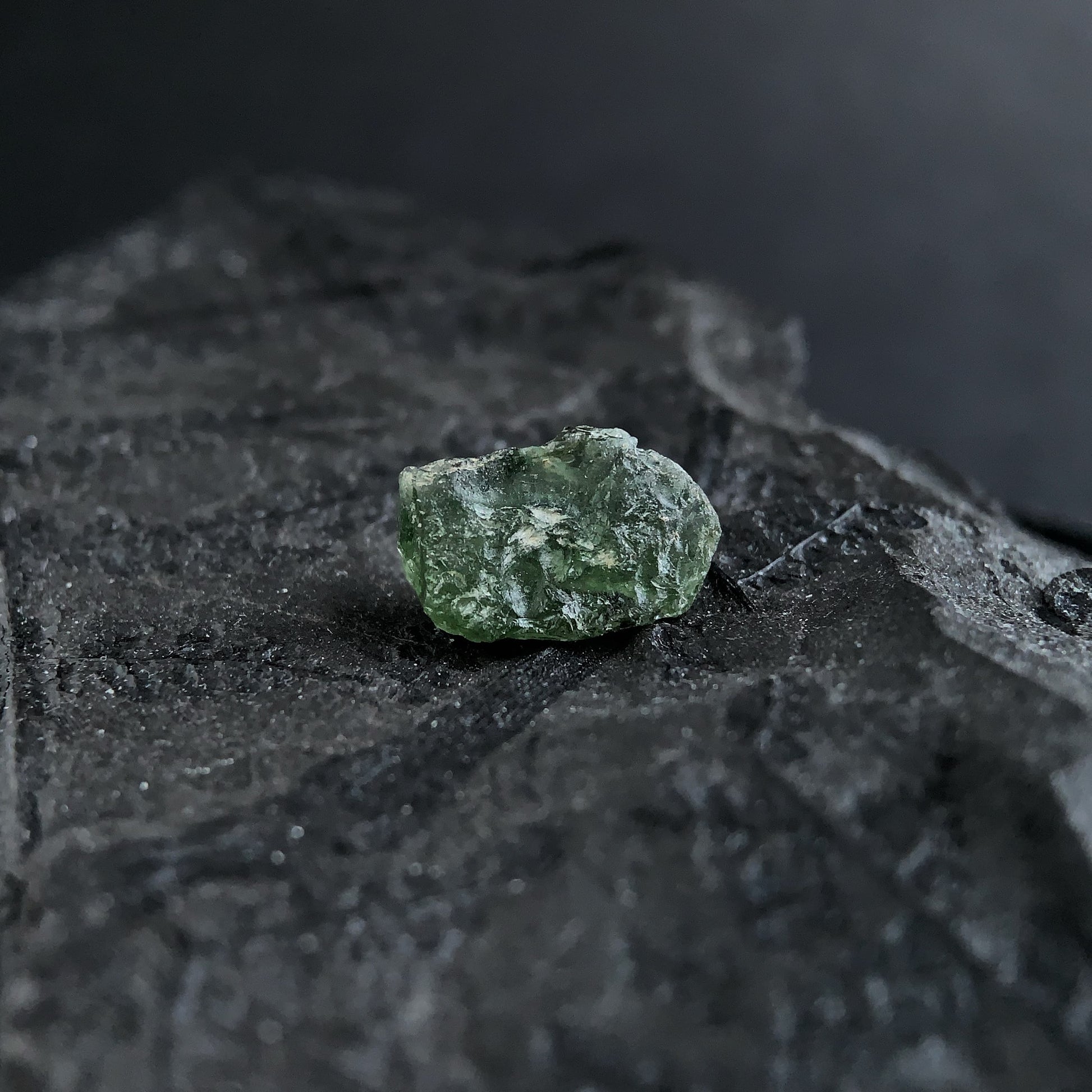 raw moldavite on a textured black surface with a dark background