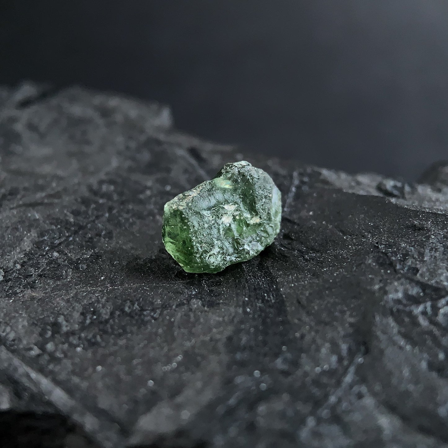 raw moldavite on a textured black surface with a dark background