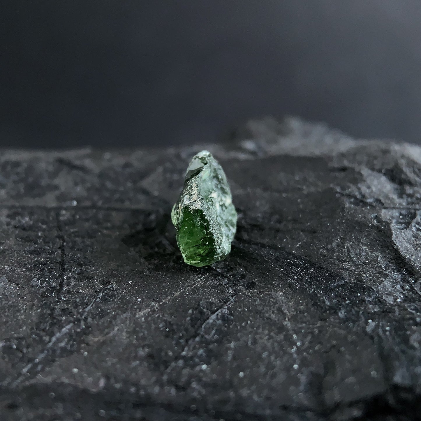 raw moldavite on a textured black surface with a dark background
