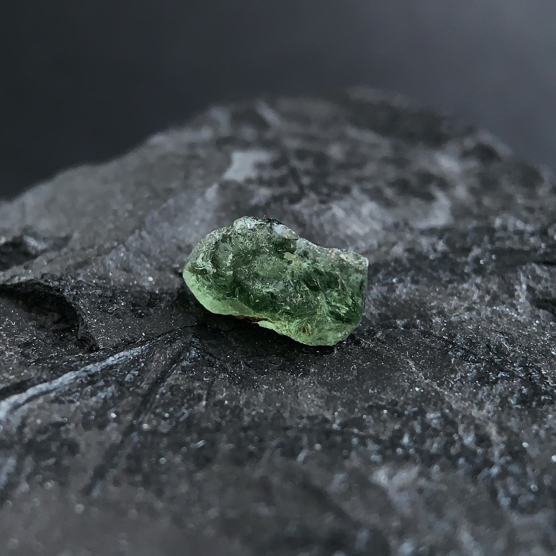 raw moldavite on a textured black surface with a dark background