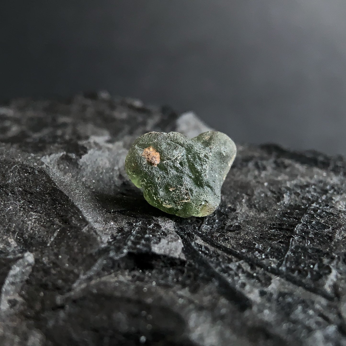 raw moldavite on a textured black surface with a dark background