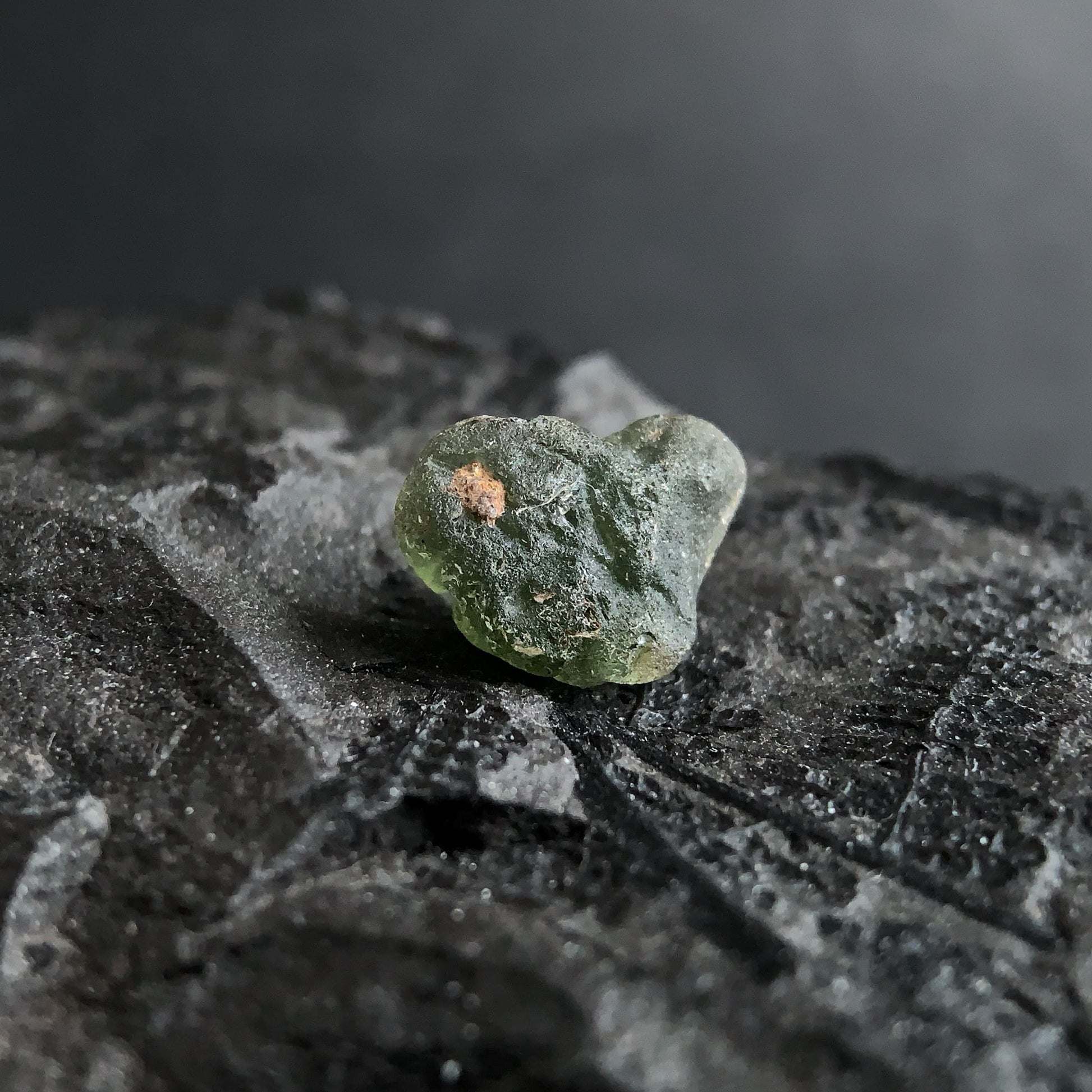 raw moldavite on a textured black surface with a dark background