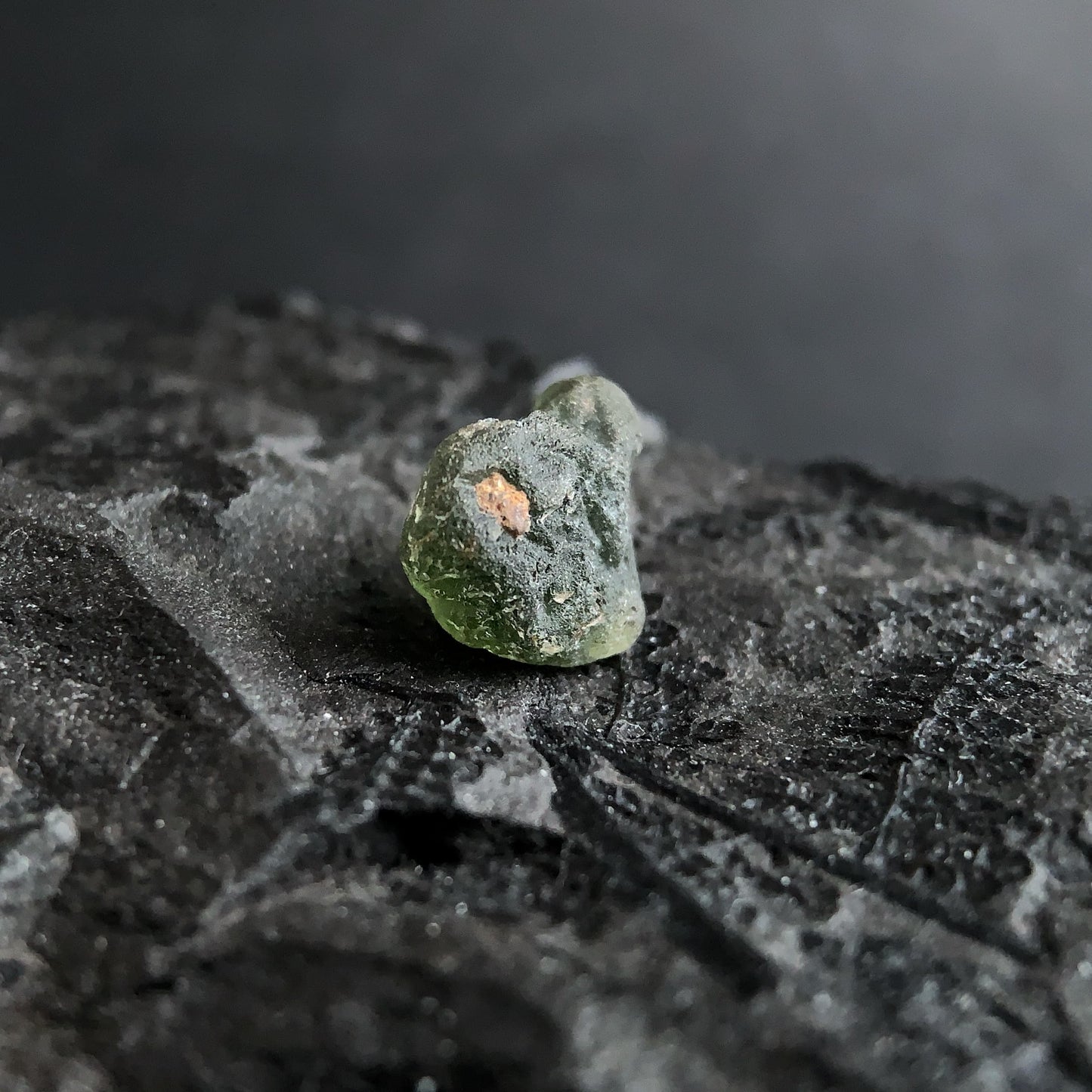 raw moldavite on a textured black surface with a dark background