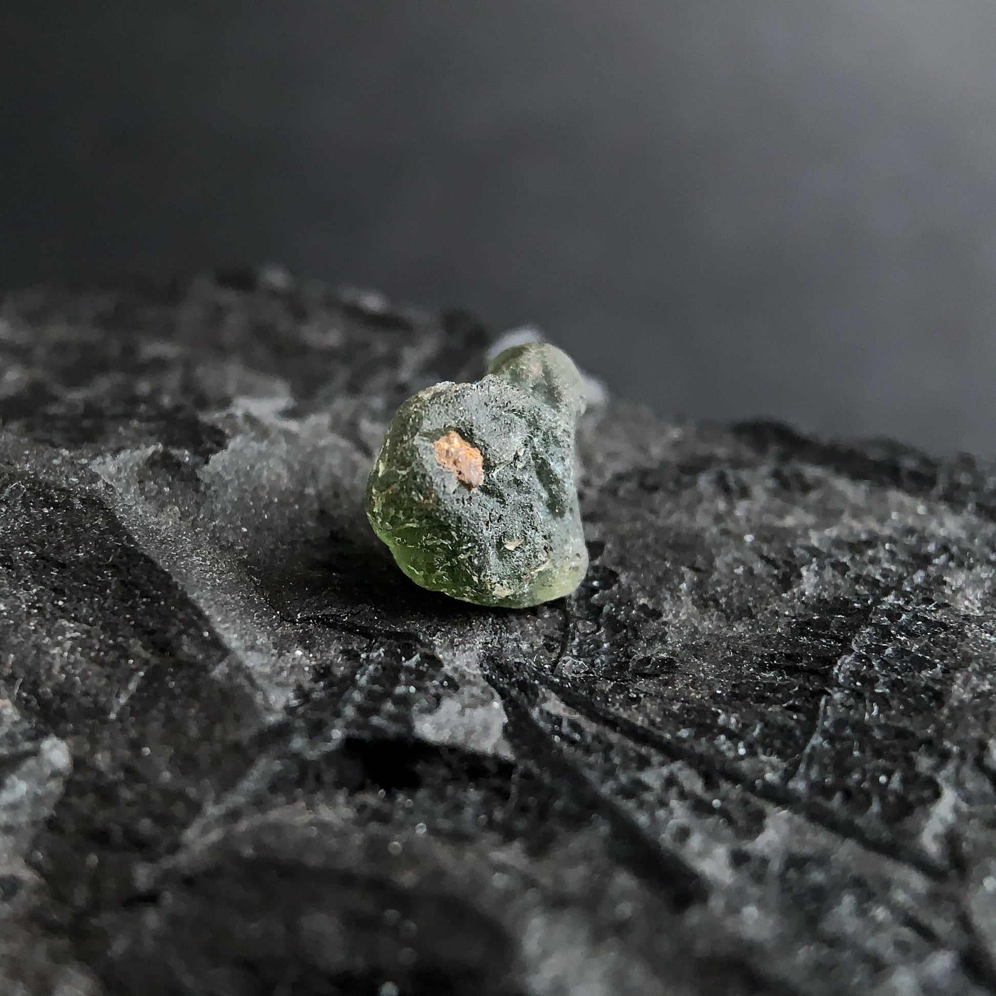 raw moldavite on a textured black surface with a dark background