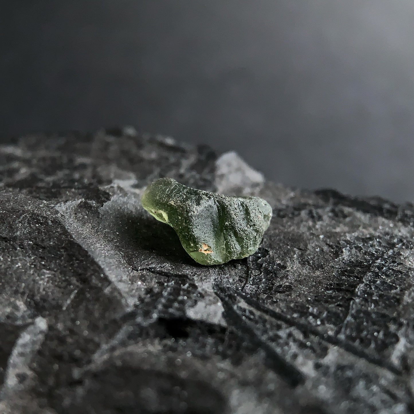 raw moldavite on a textured black surface with a dark background