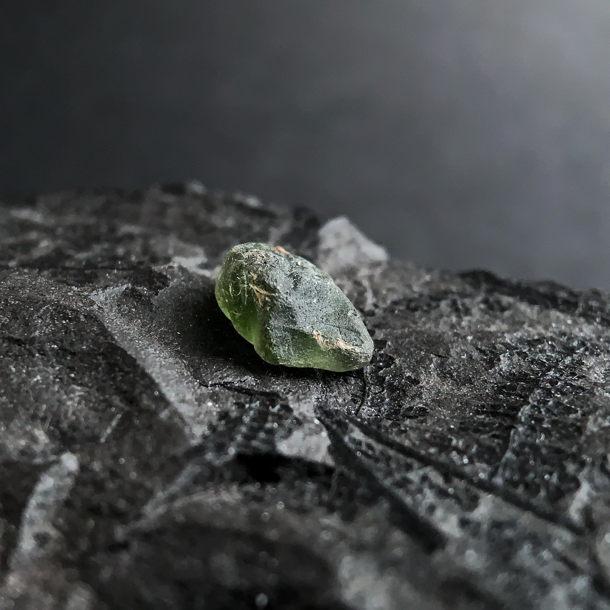 raw moldavite on a textured black surface with a dark background
