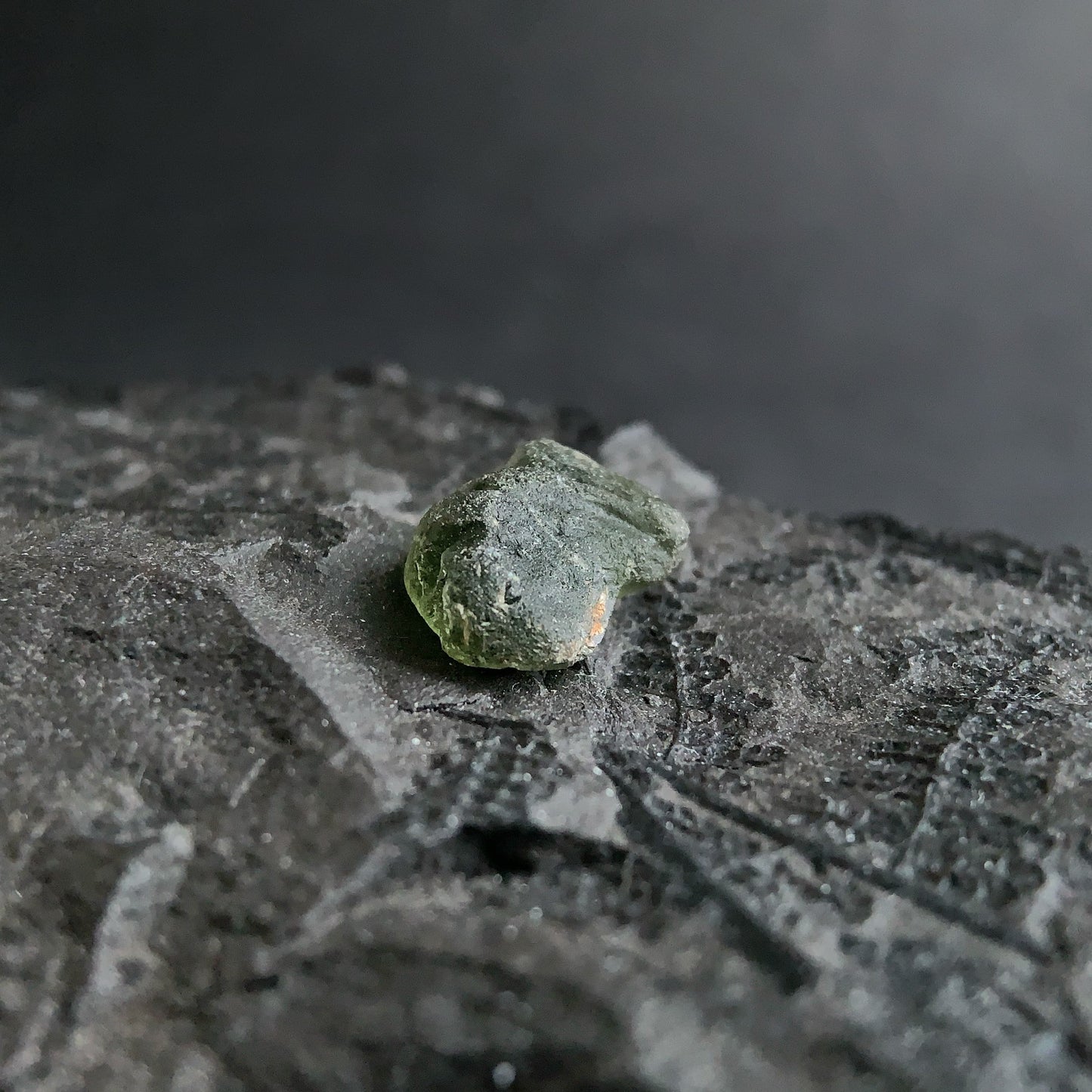 raw moldavite on a textured black surface with a dark background