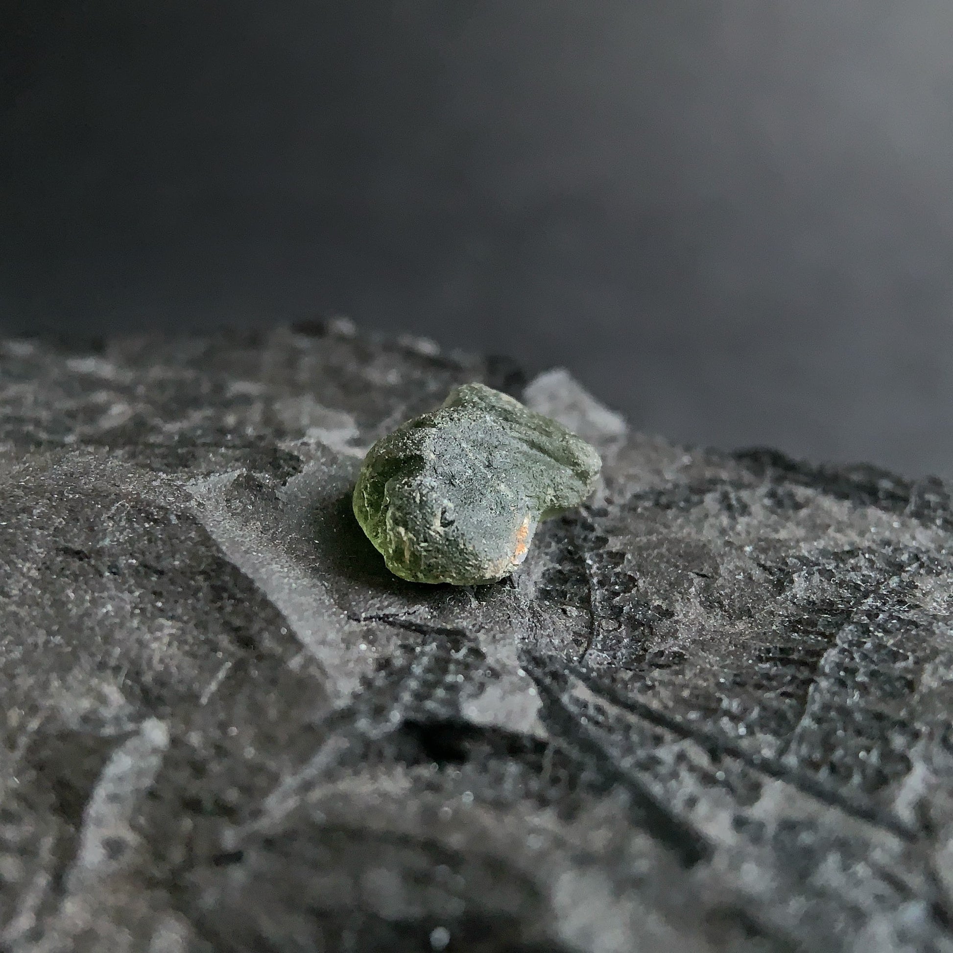 raw moldavite on a textured black surface with a dark background