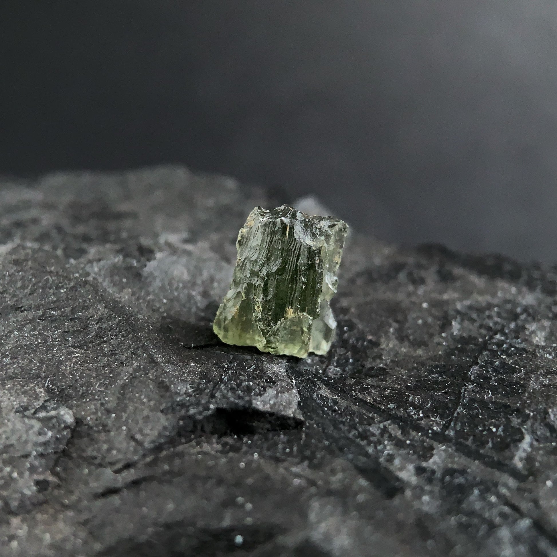 raw moldavite on a textured black surface with a dark background