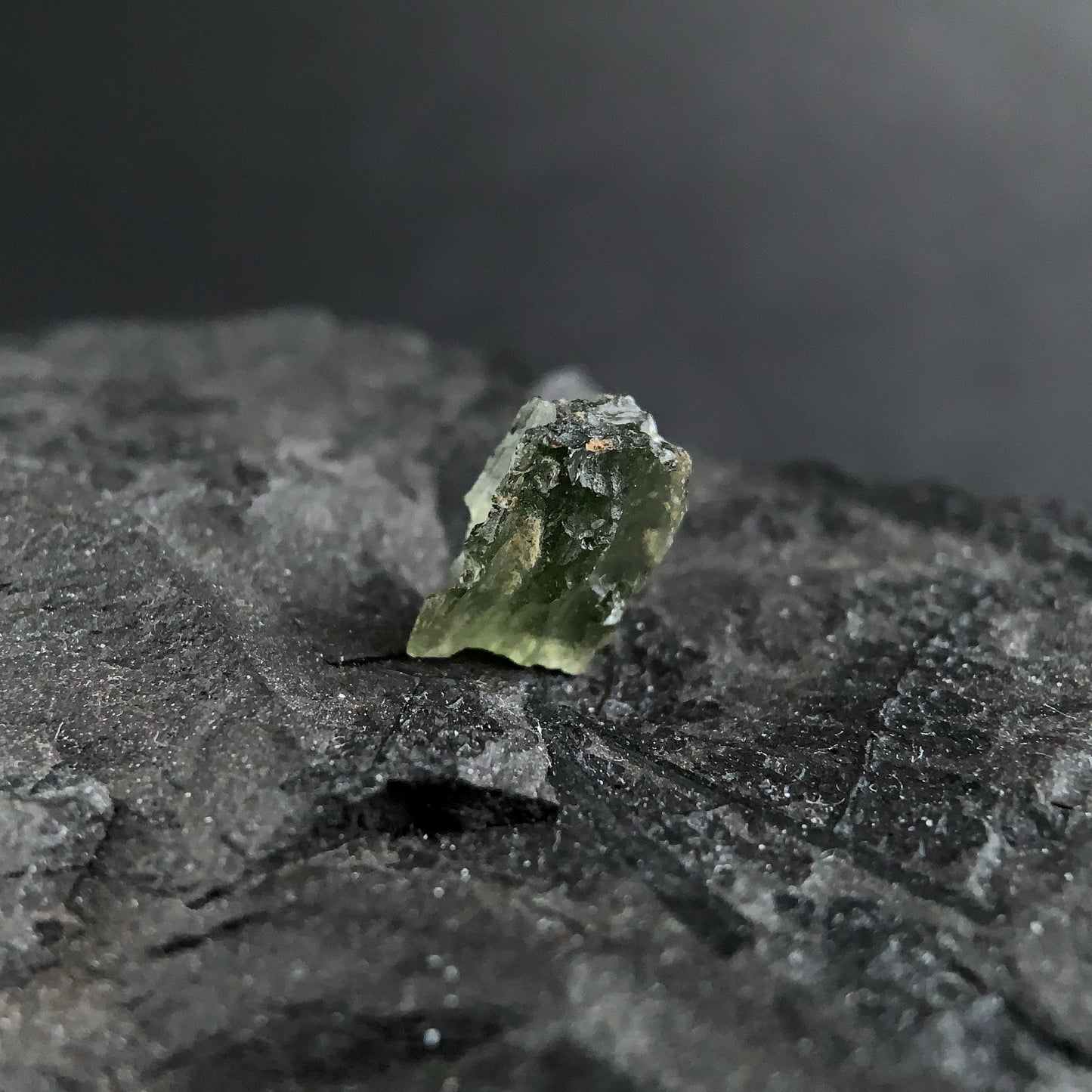 raw moldavite on a textured black surface with a dark background