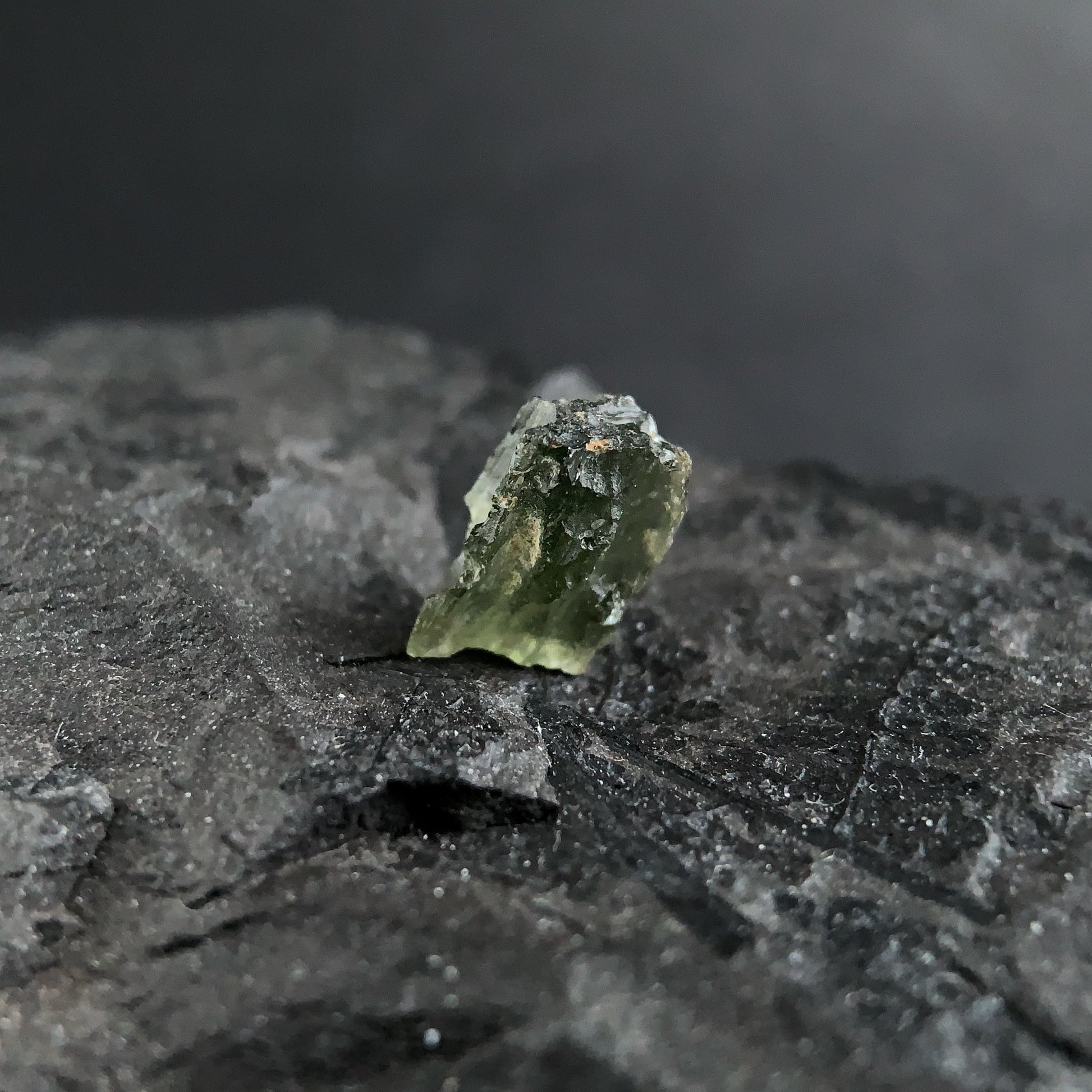 raw moldavite on a textured black surface with a dark background
