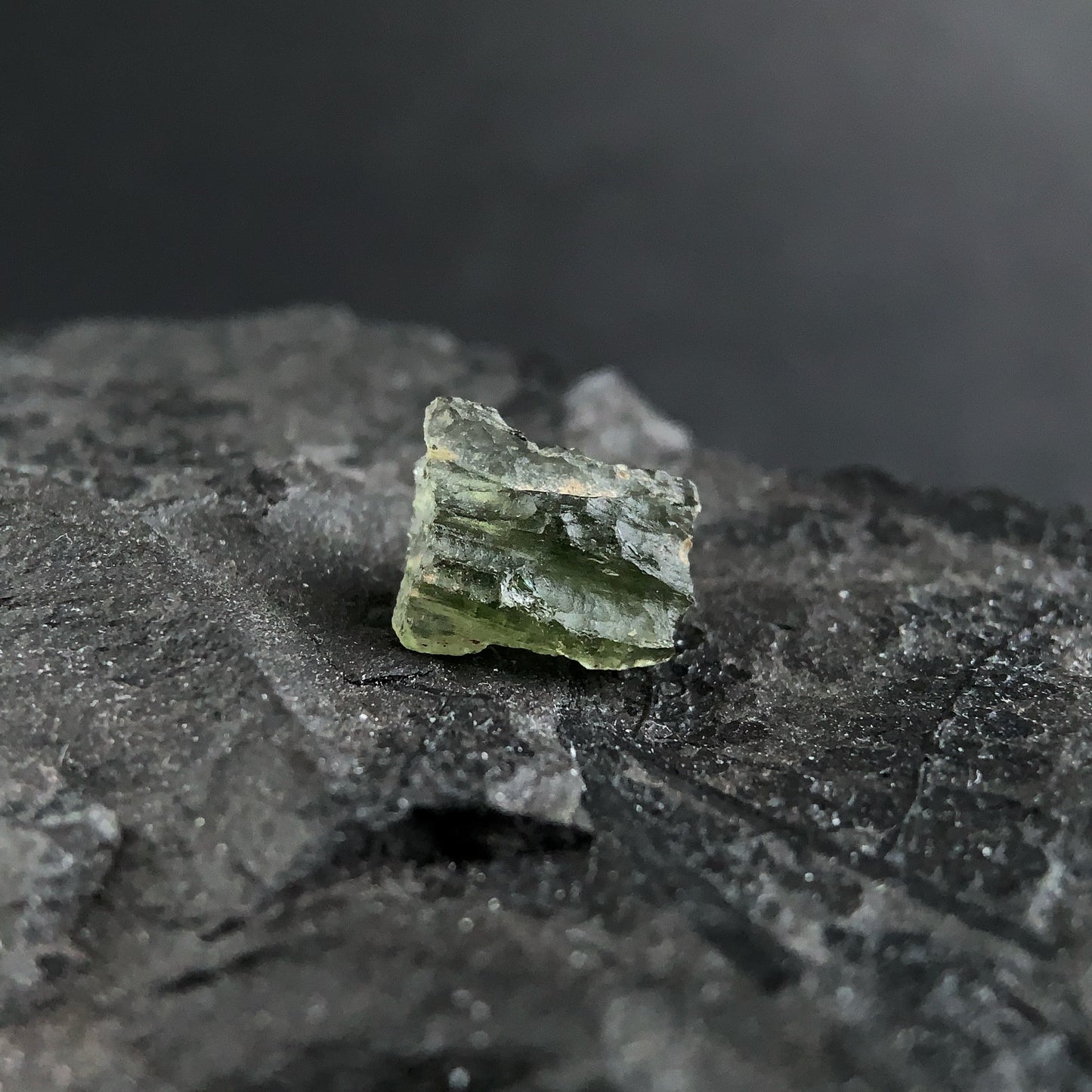 raw moldavite on a textured black surface with a dark background