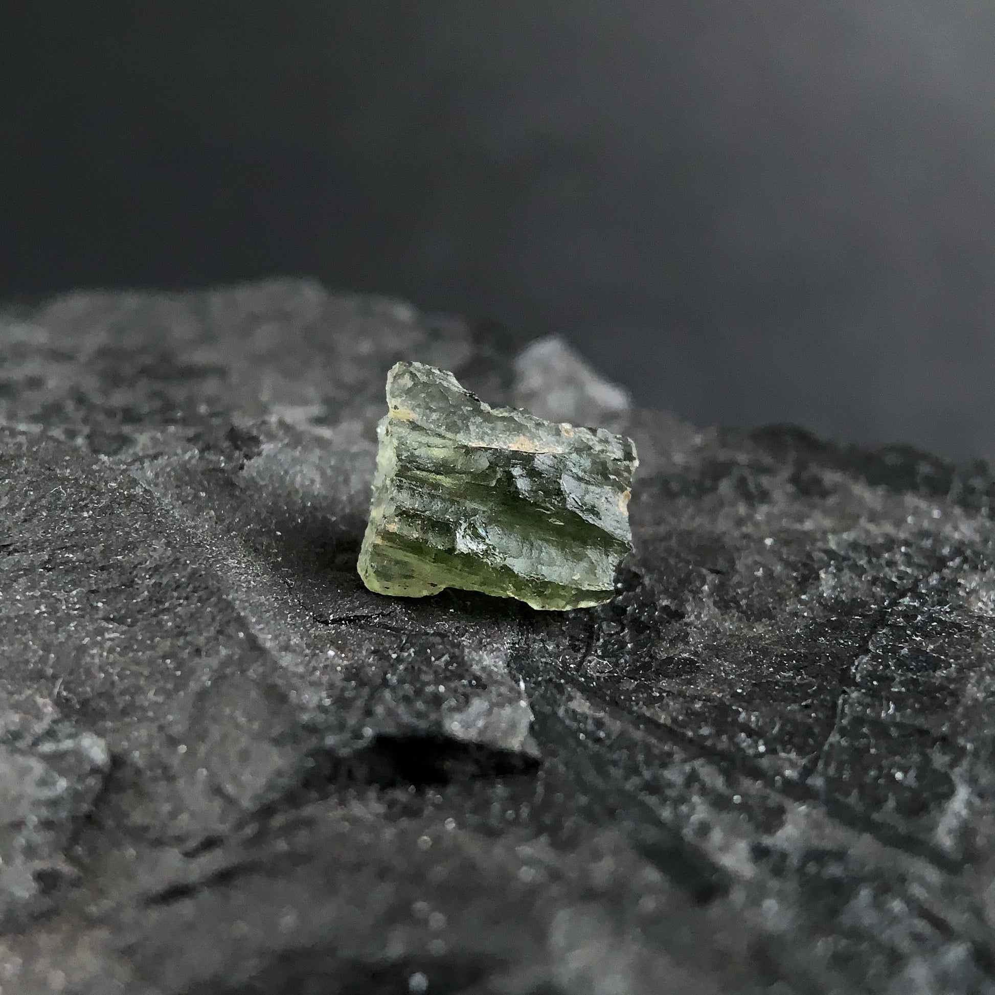 raw moldavite on a textured black surface with a dark background
