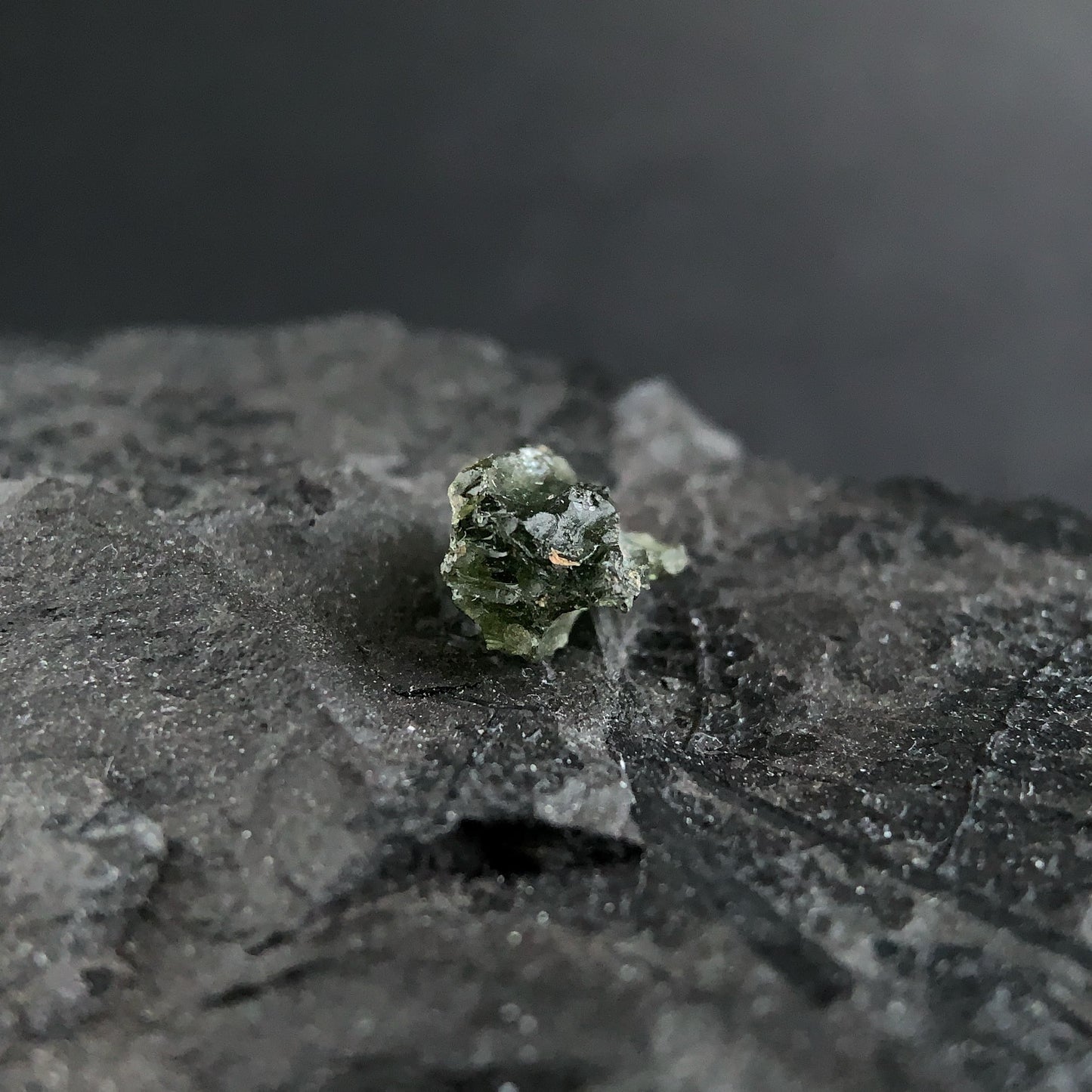 raw moldavite on a textured black surface with a dark background