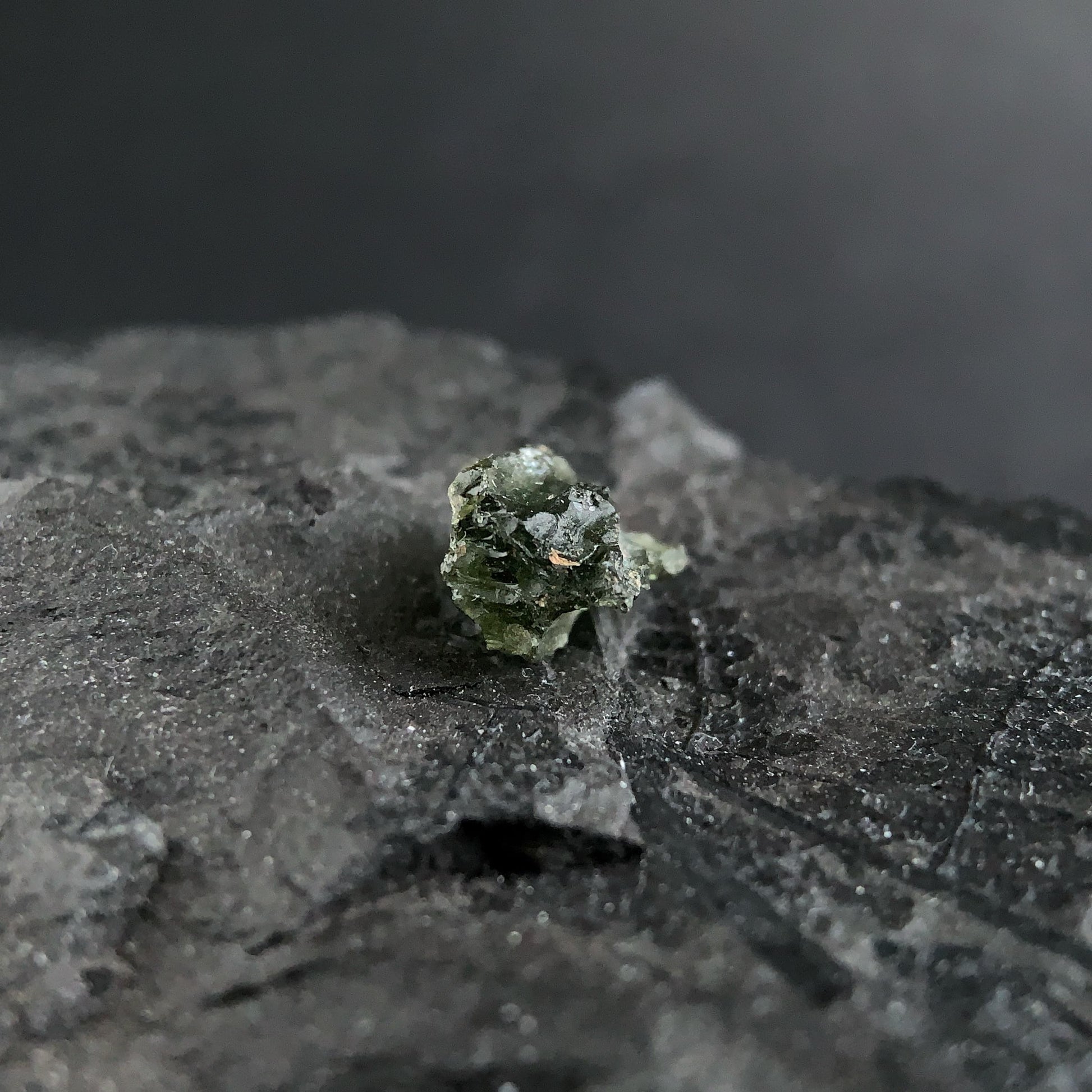 raw moldavite on a textured black surface with a dark background