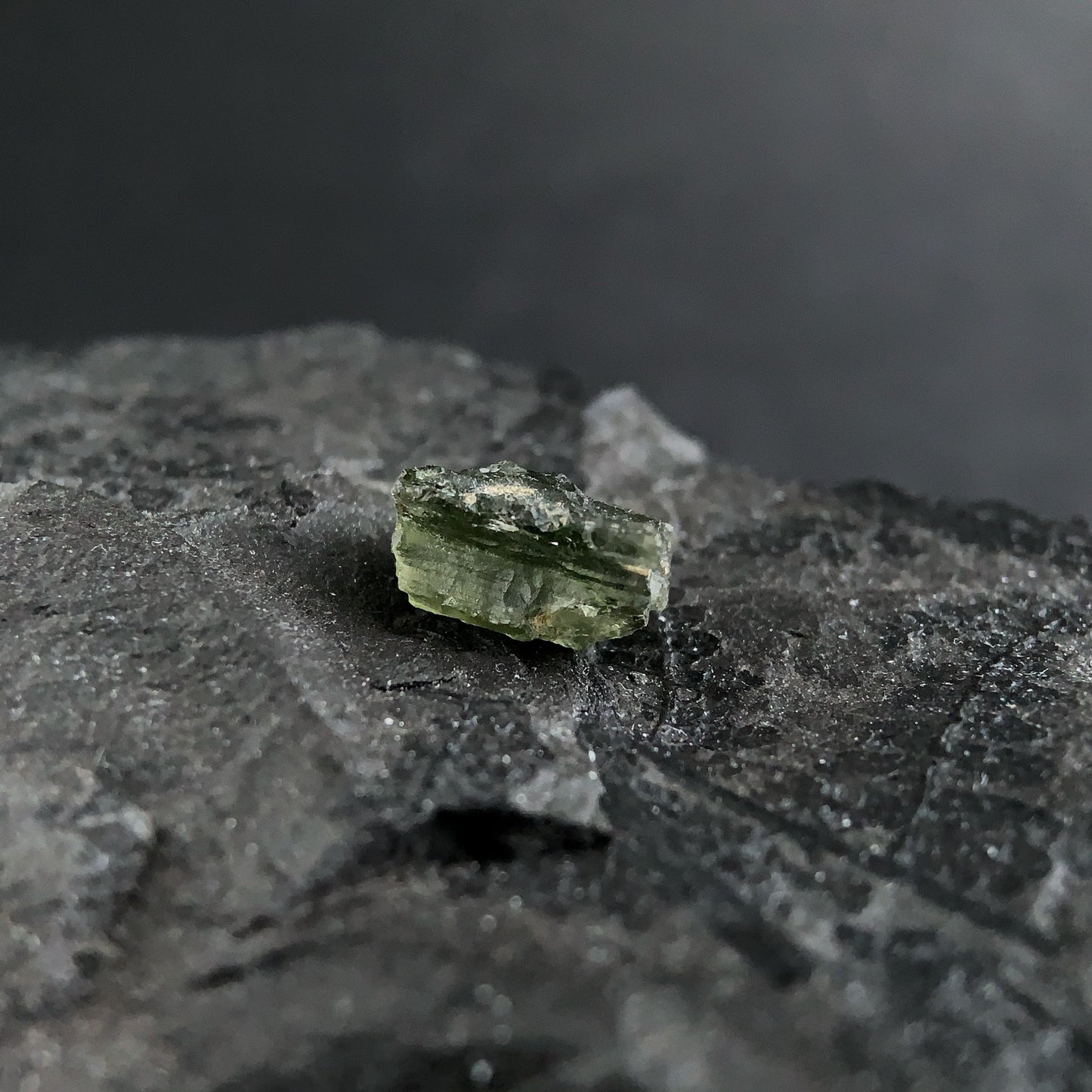 raw moldavite on a textured black surface with a dark background