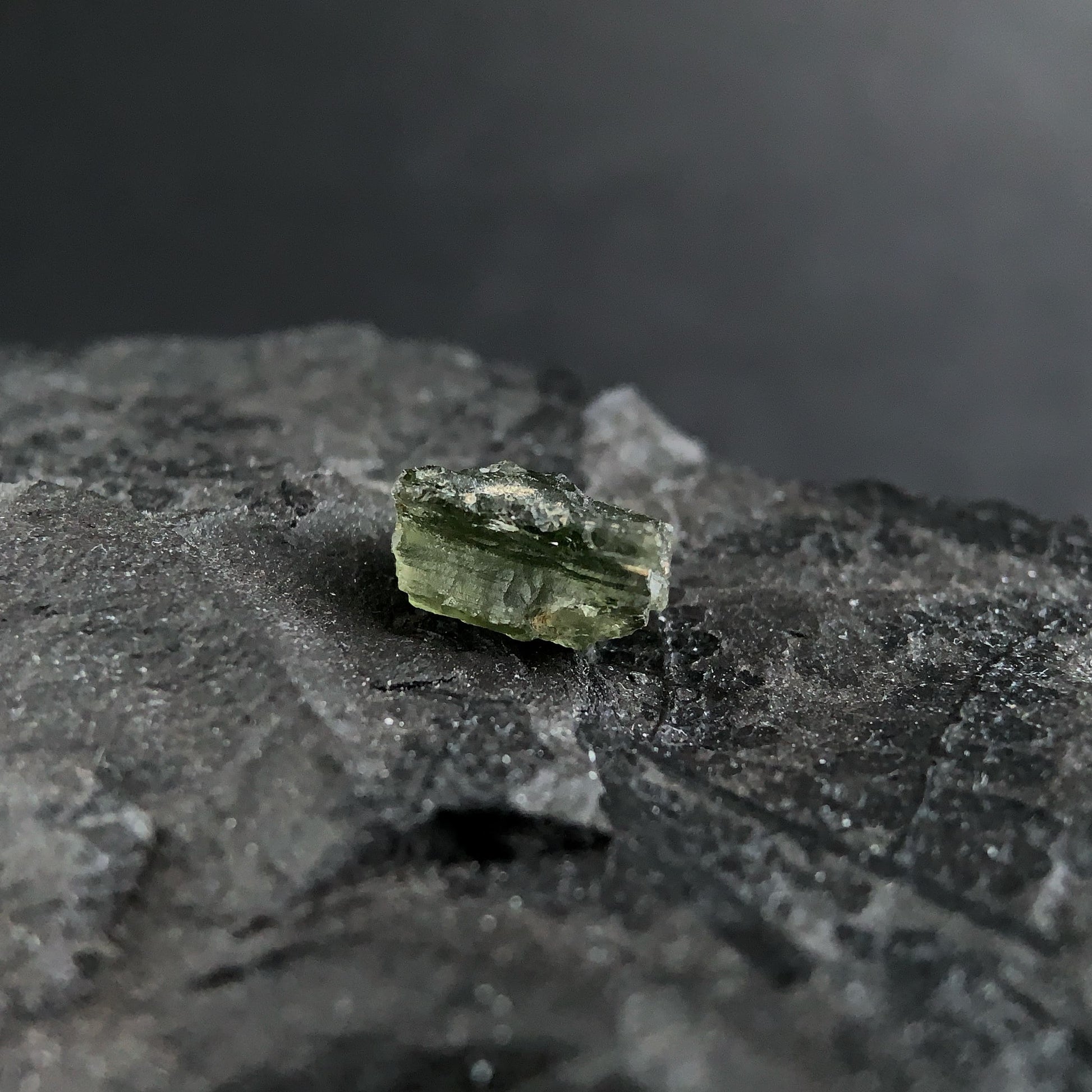 raw moldavite on a textured black surface with a dark background