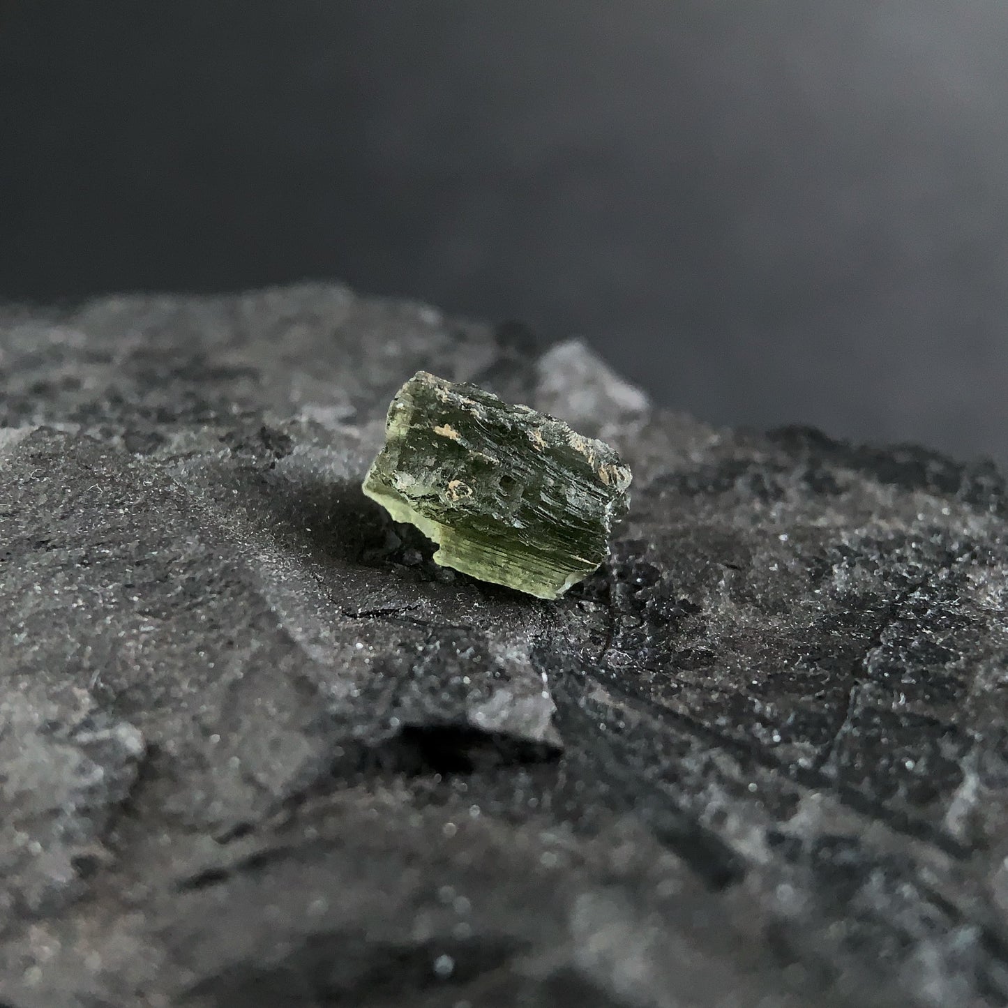 raw moldavite on a textured black surface with a dark background