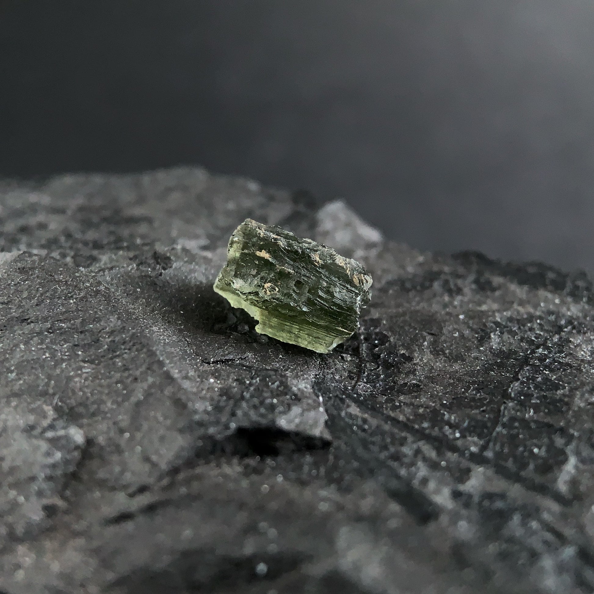 raw moldavite on a textured black surface with a dark background