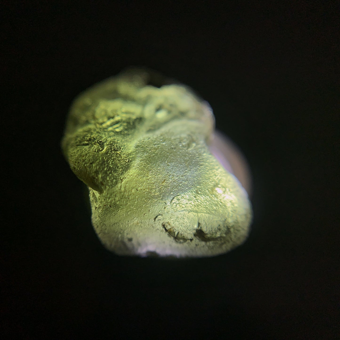 Close-up of a raw moldavite crystal on a black background