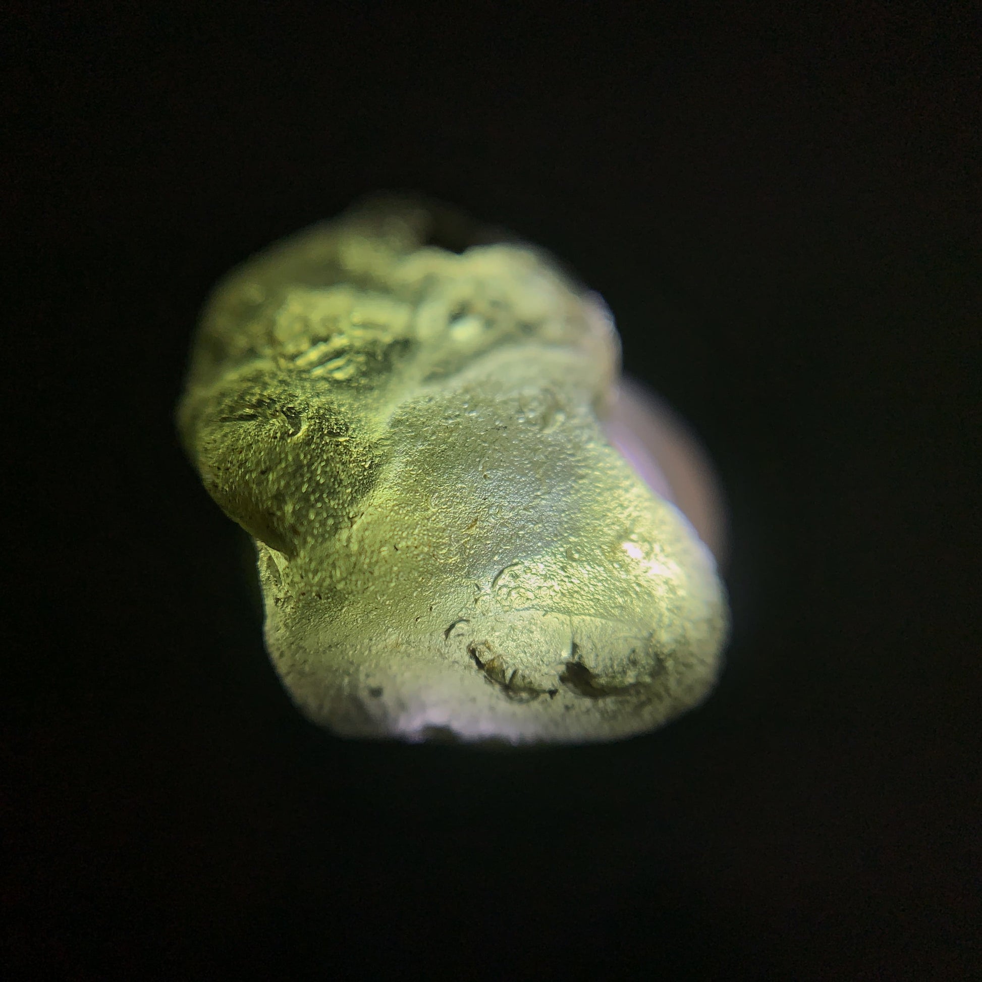 Close-up of a raw moldavite crystal on a black background