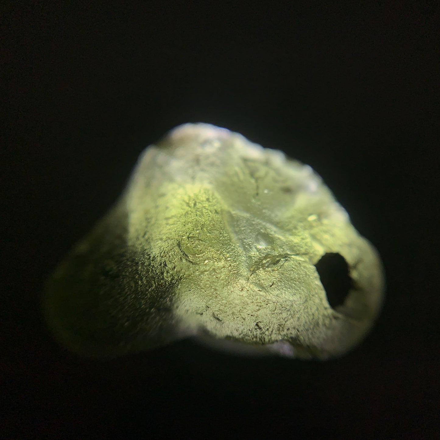 Close-up of a raw moldavite crystal on a black background