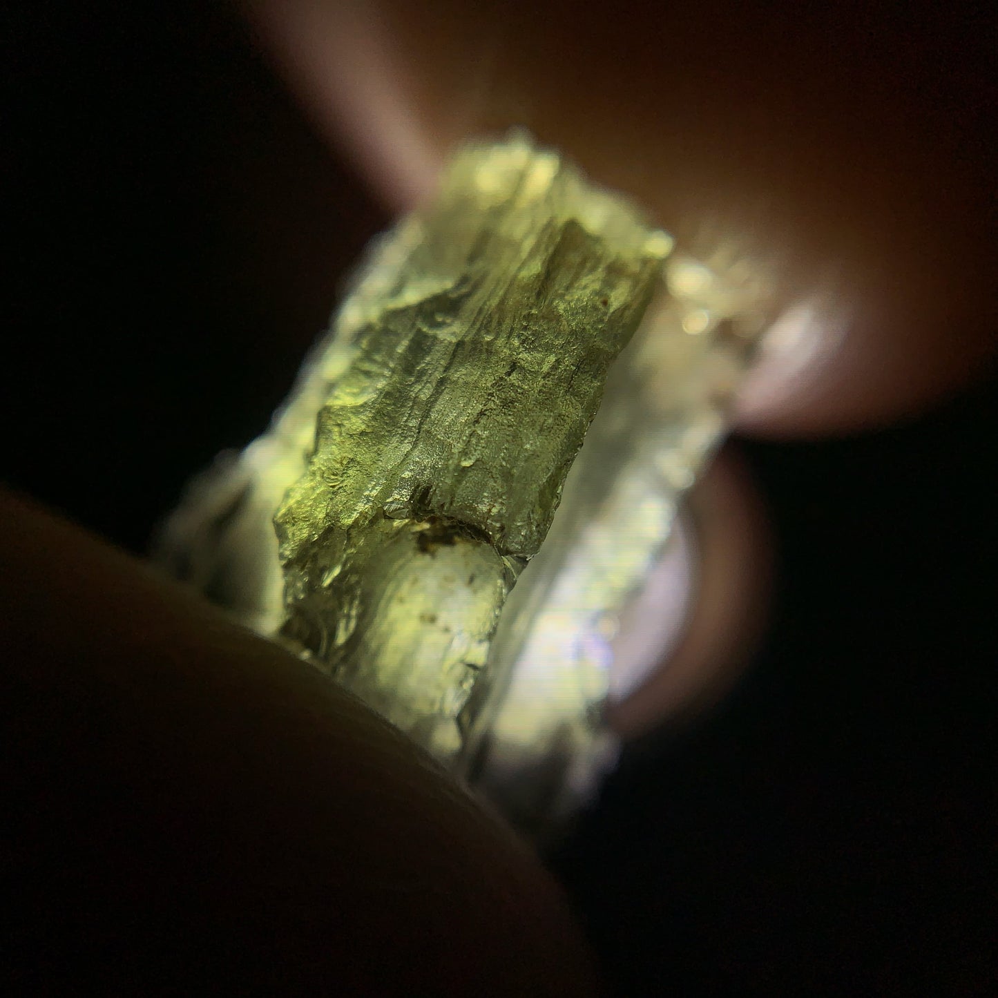 Close-up of a moldavite crystal held between fingers against a dark background