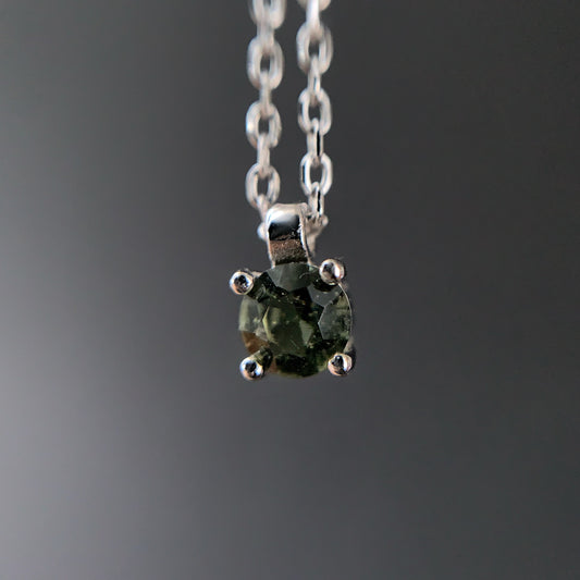 Close-up shot of Moldavite pendant on a Sterling silver chain against a dark background