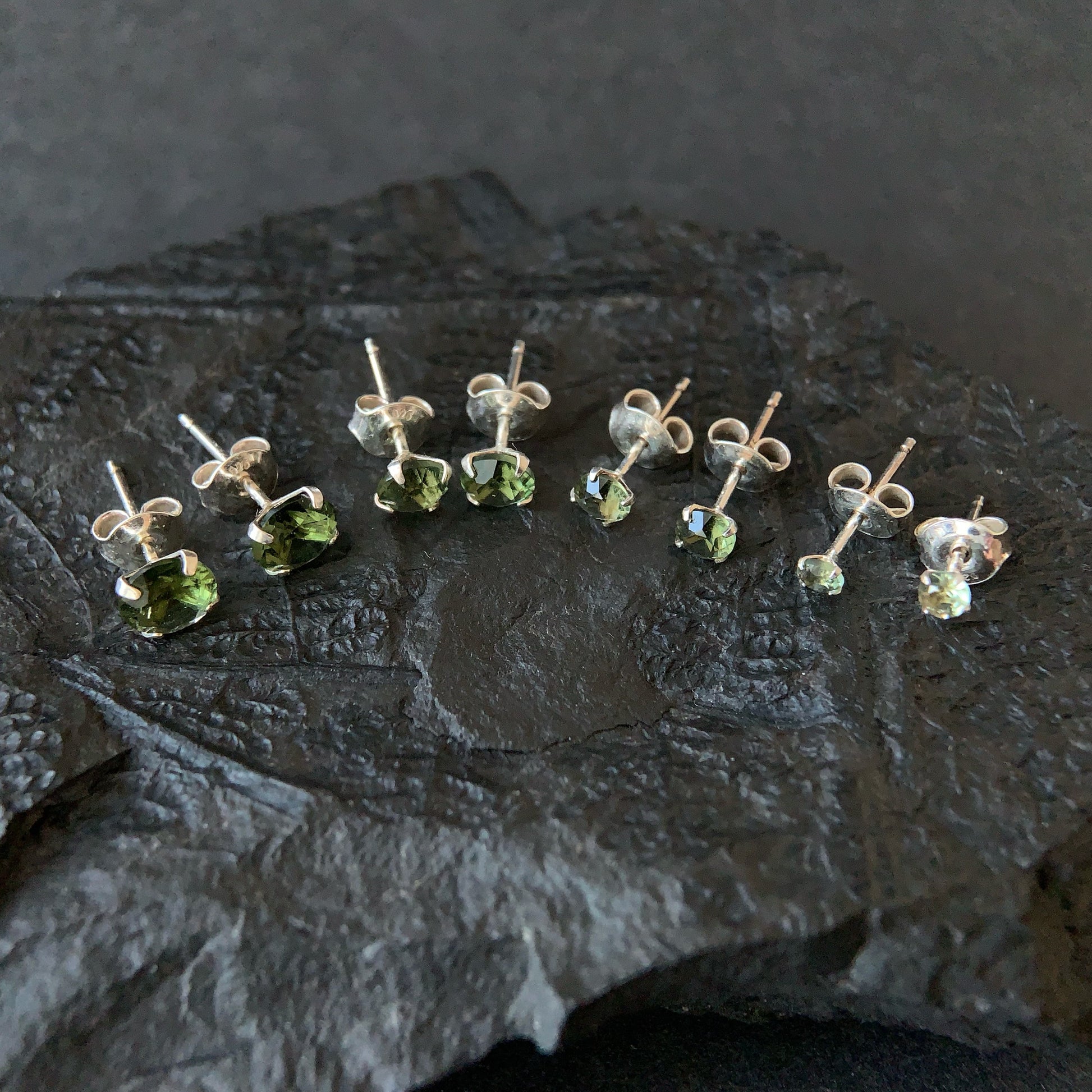 Set of different Moldavite earrings on a dark stone surface
