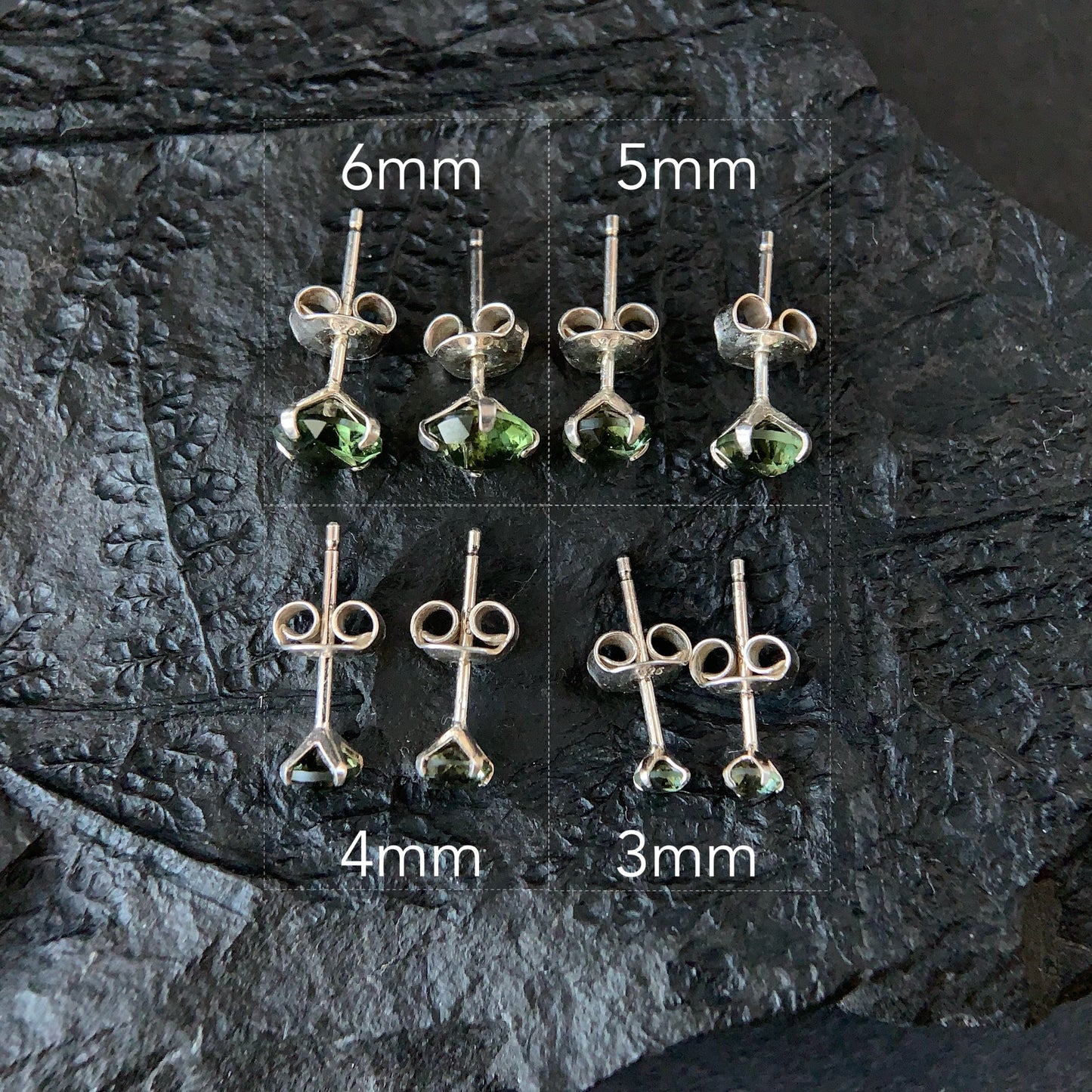 Set of Moldavite earrings with varying sizes on a dark stone surface