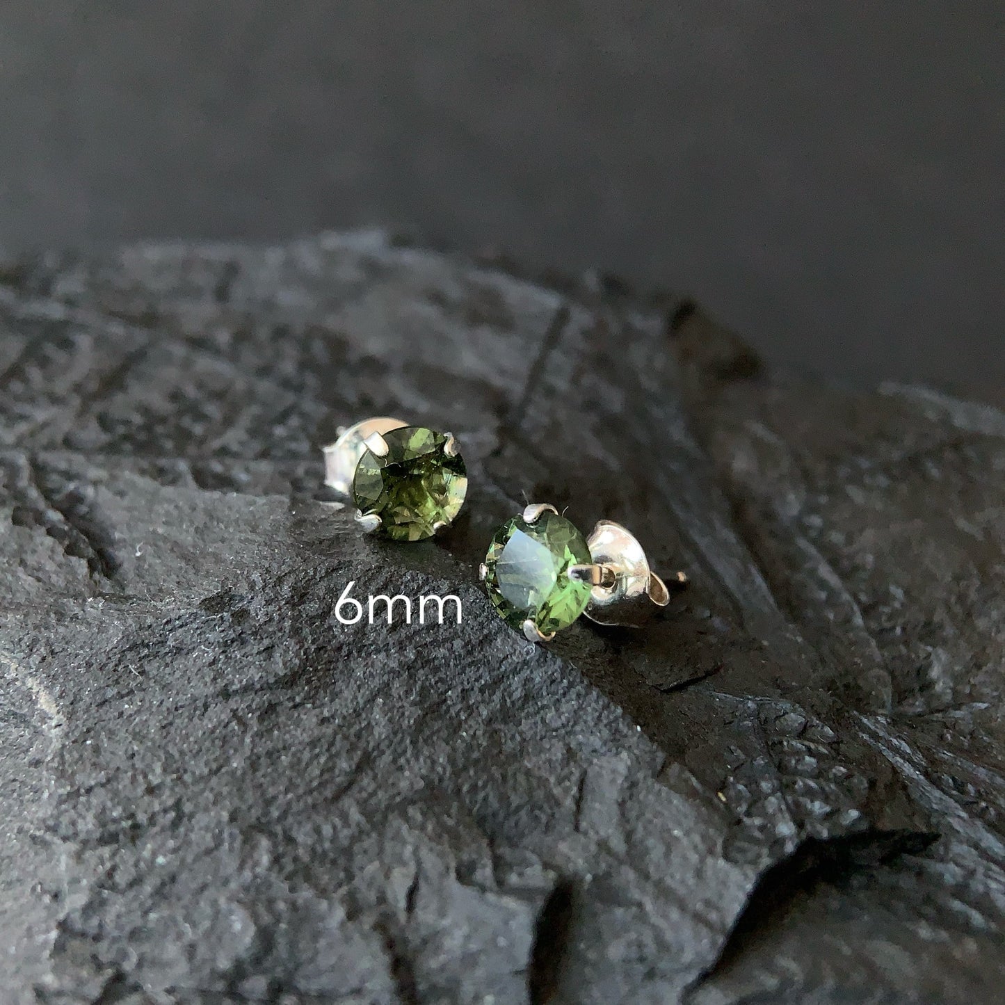 Pair of Moldavite stud earrings on a textured dark surface with '6mm' text.