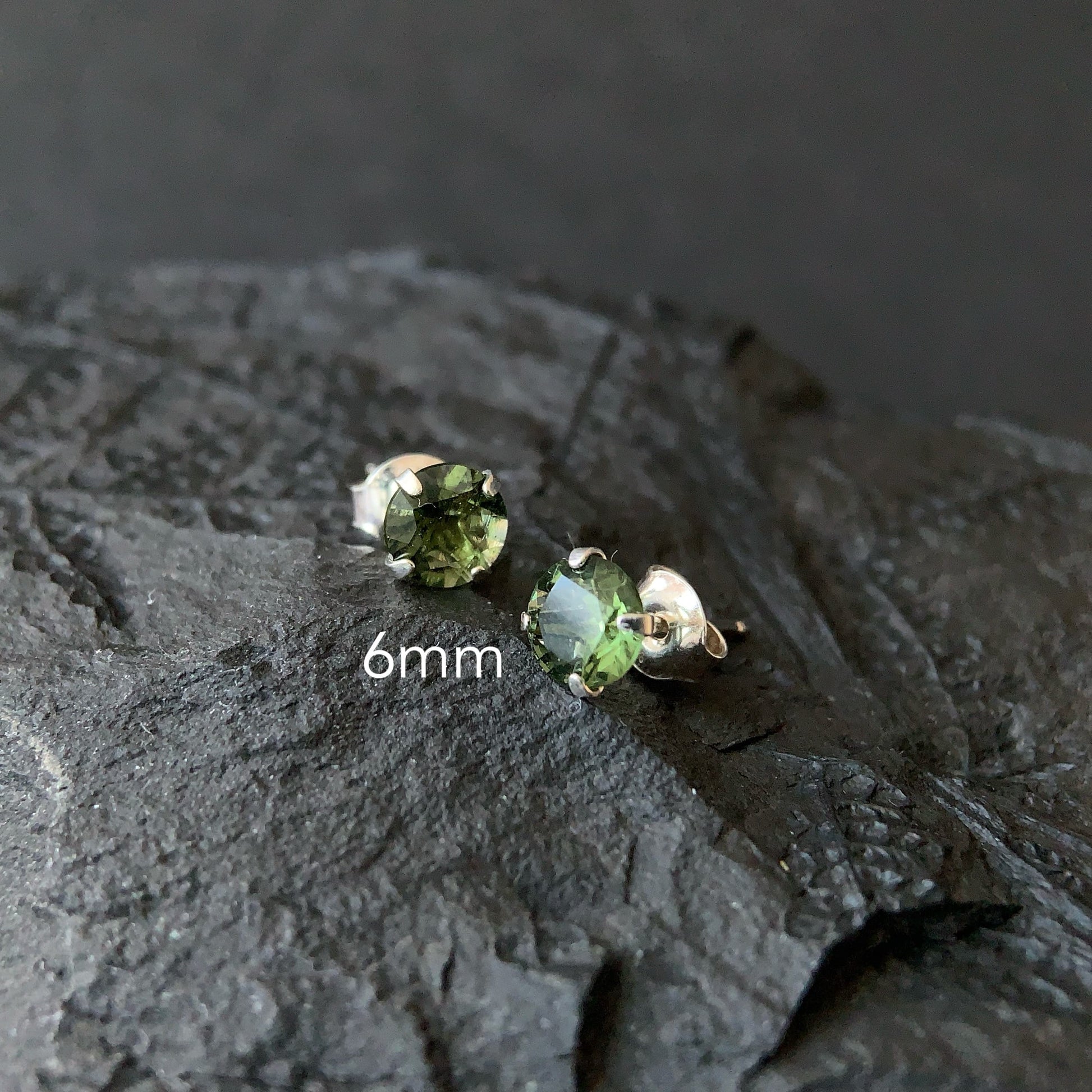 Pair of Moldavite stud earrings on a textured dark surface with '6mm' text.