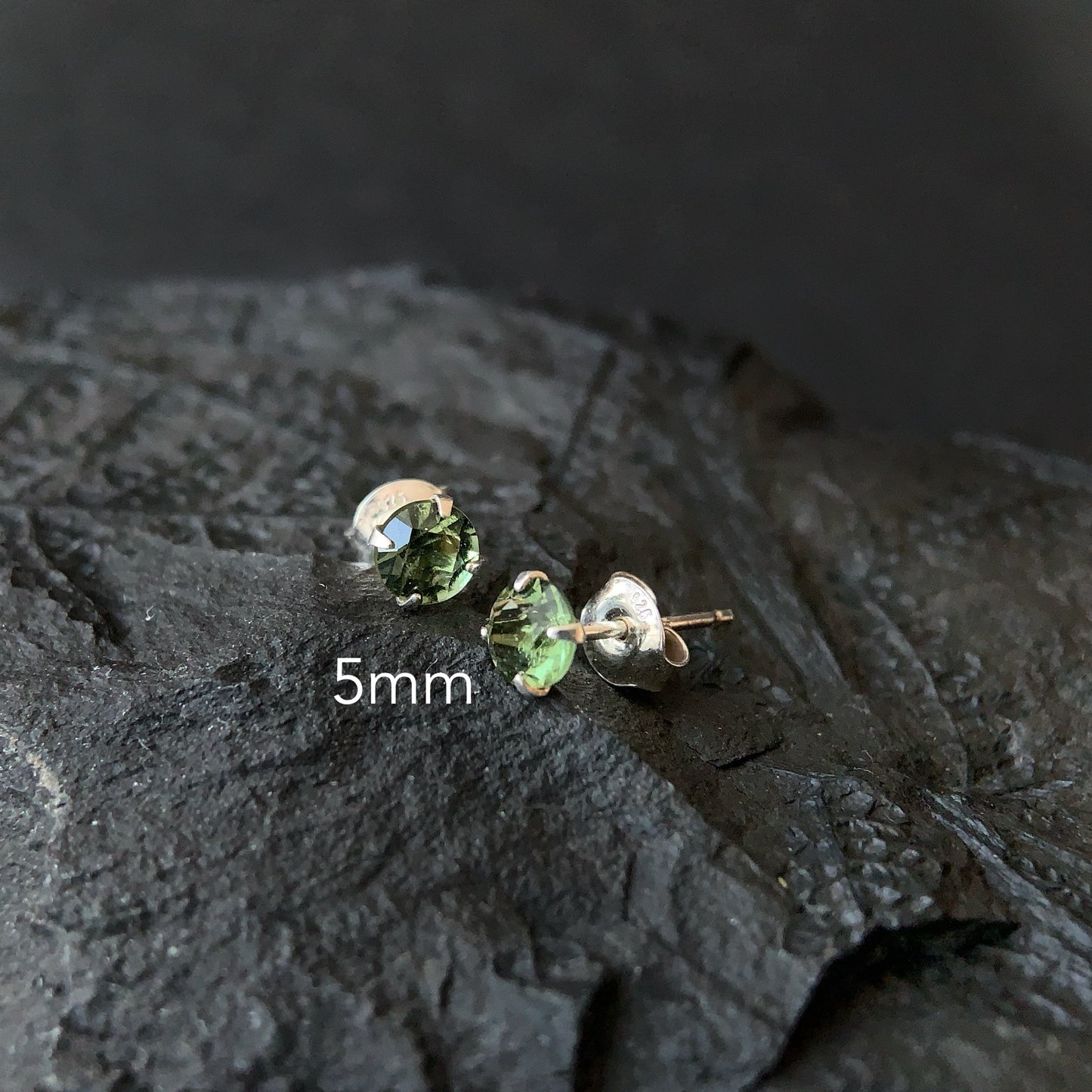 Moldavite stud earrings on a dark textured surface with '5mm' text.