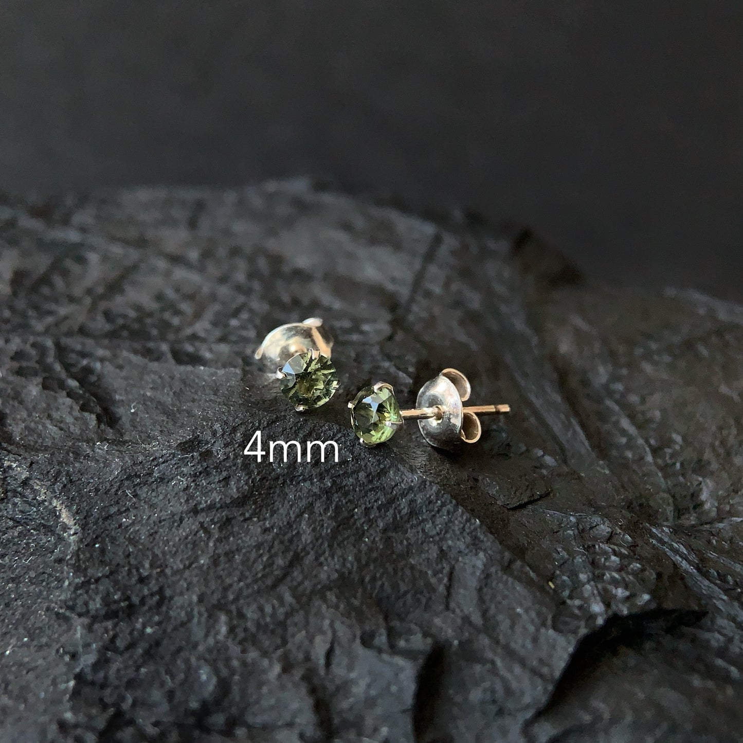 Pair of 4mm Moldavite stud earrings on a textured dark surface