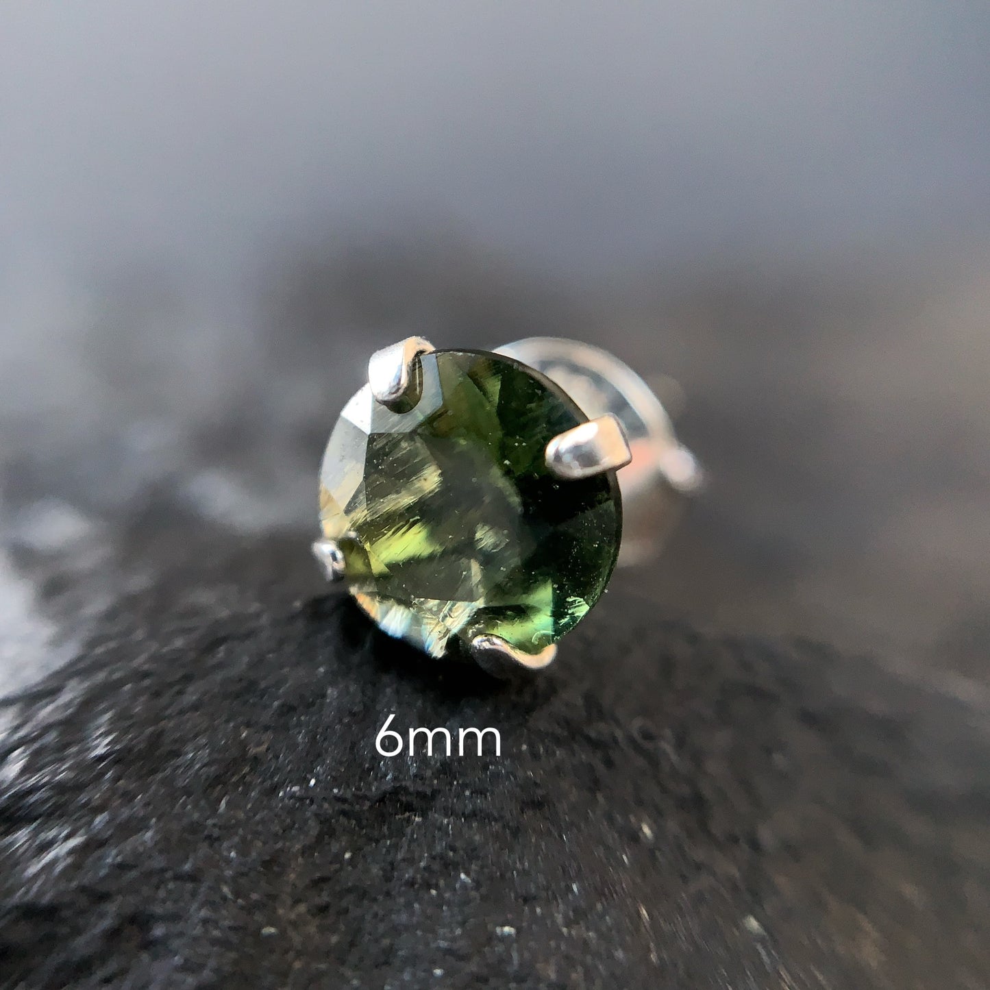 Macro shot of Moldavite stud earring on a dark textured surface with '6mm' text.