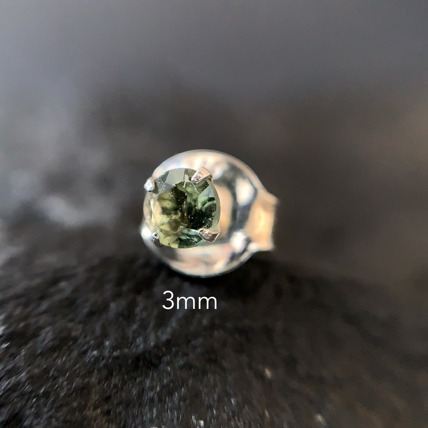 Silver stud earring with a 3mm moldavite on a dark textured surface