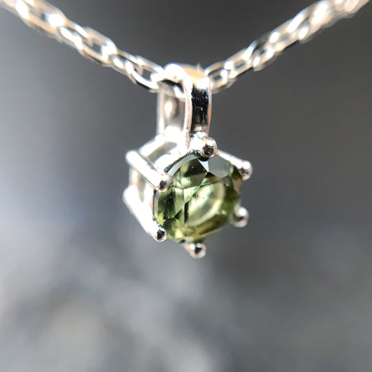 Macro shot 5mm Moldavite pendant on a silver chain against a blurred background