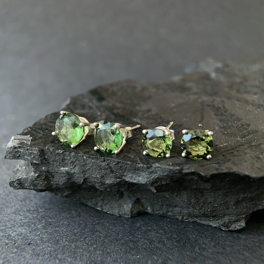 7 and 8 mm Moldavite stud earrings on a dark stone surface