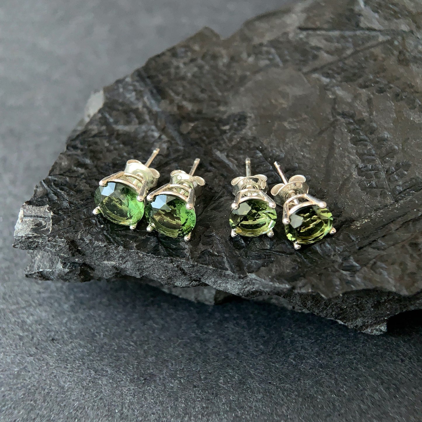 Four Moldavite stud earrings on a dark stone surface