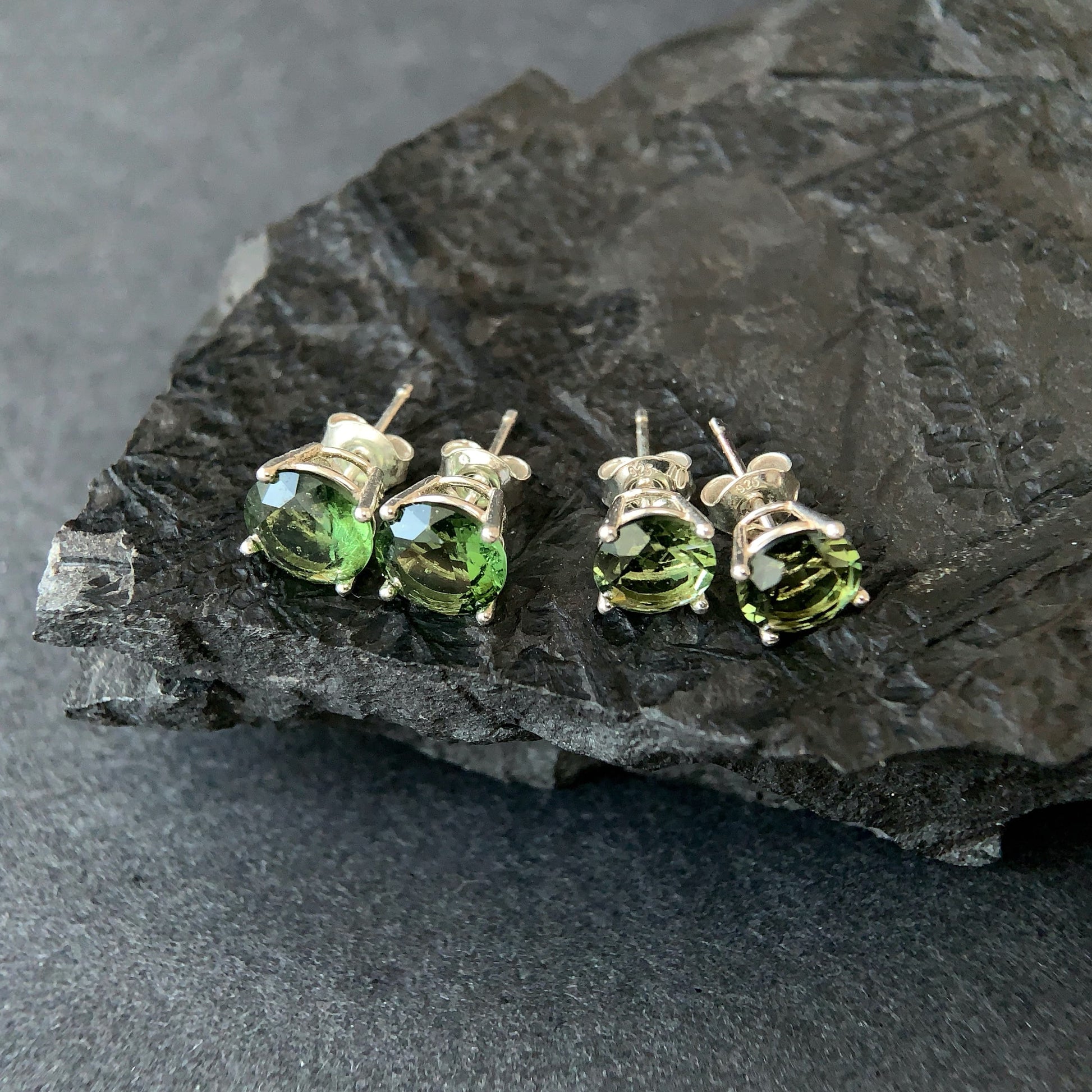 Four Moldavite stud earrings on a dark stone surface