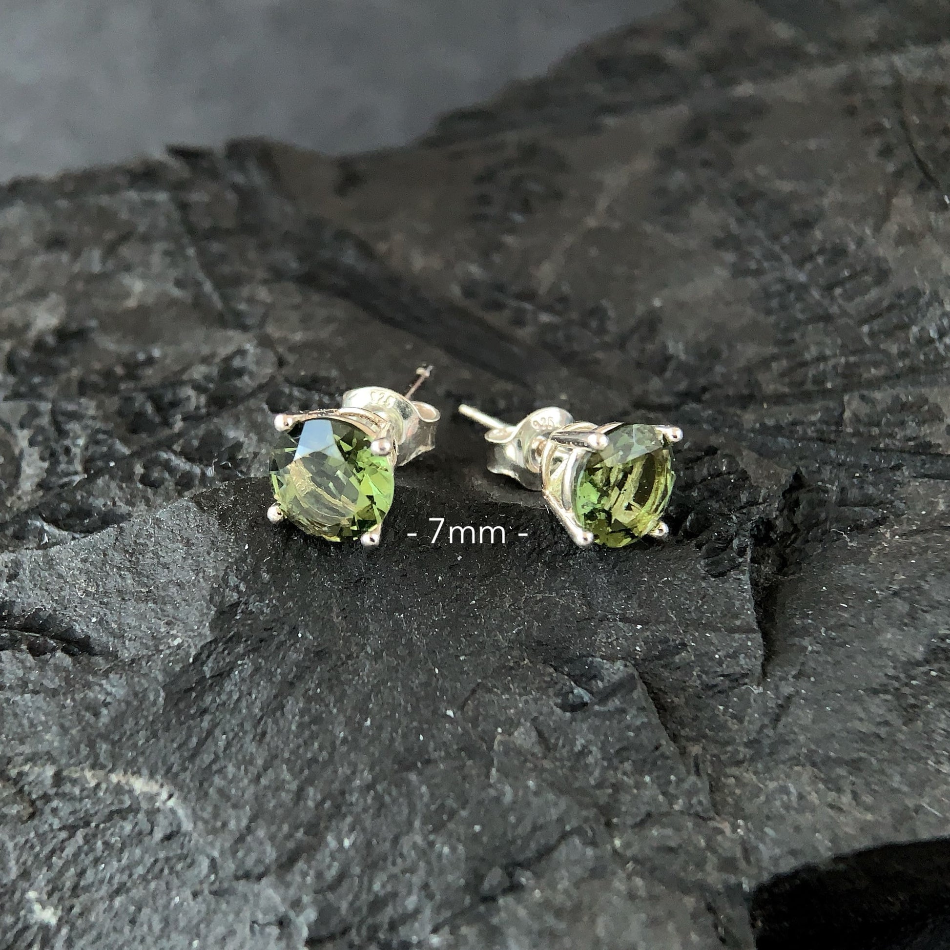 Pair of 7 mm Moldavite stud earrings on a dark stone surface
