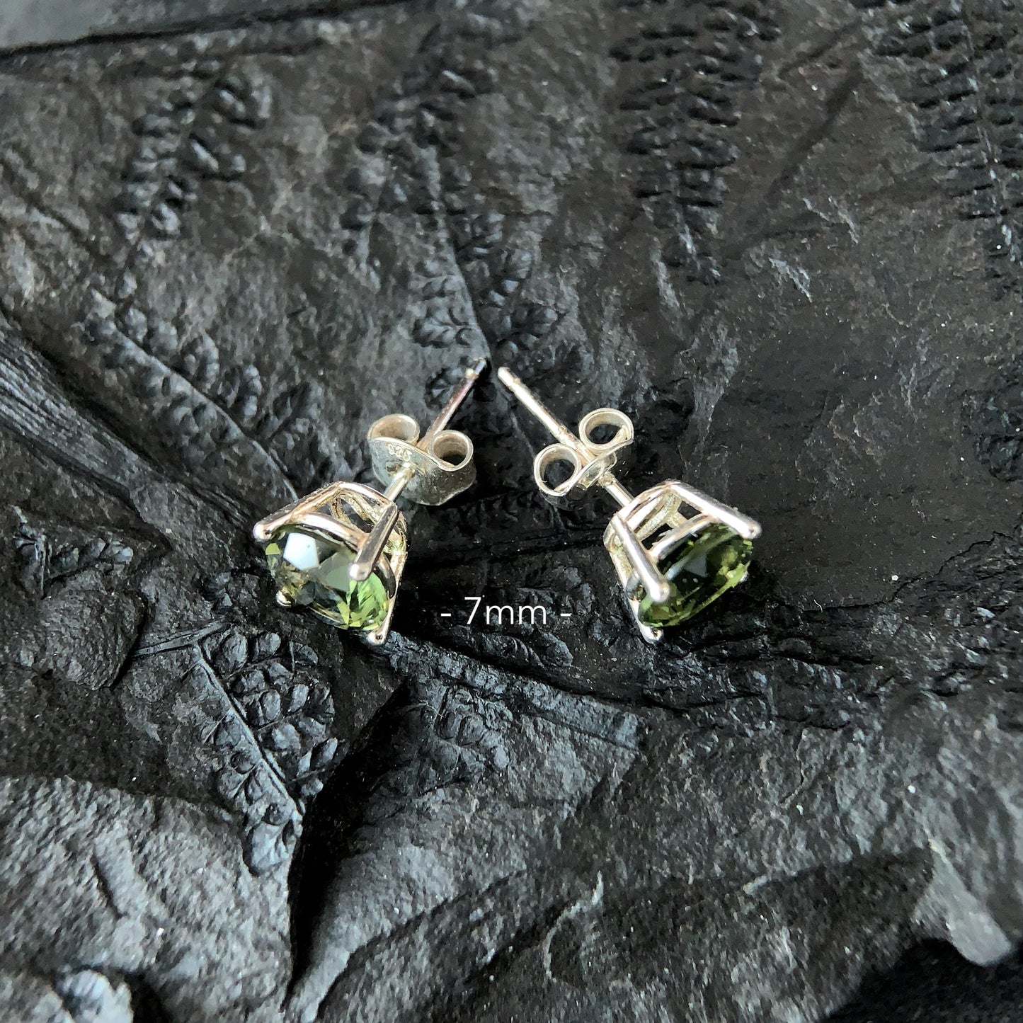 Pair of Moldavite 7mm stud earrings on a textured dark surface